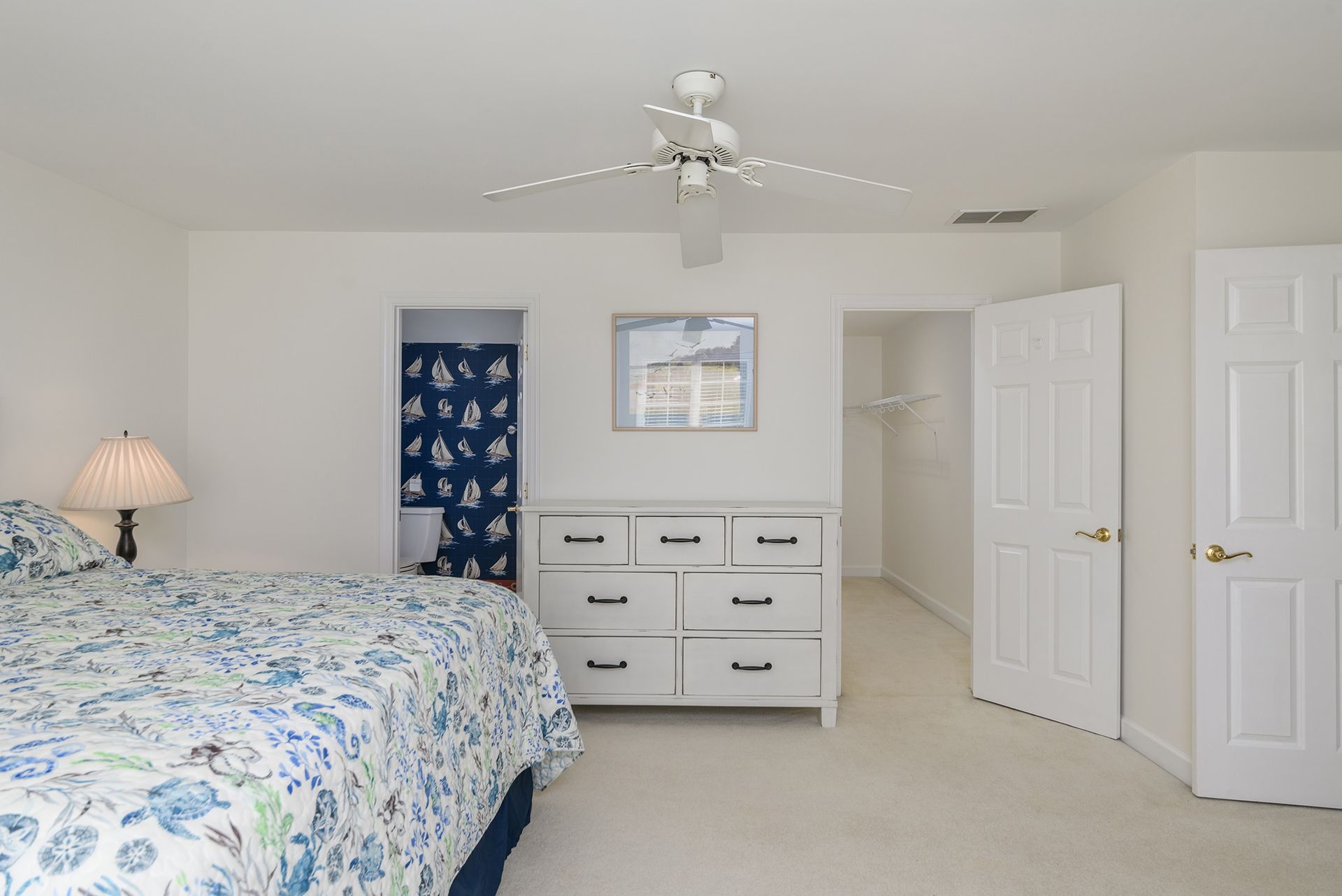 A bedroom with a bed , dresser , lamp and ceiling fan.