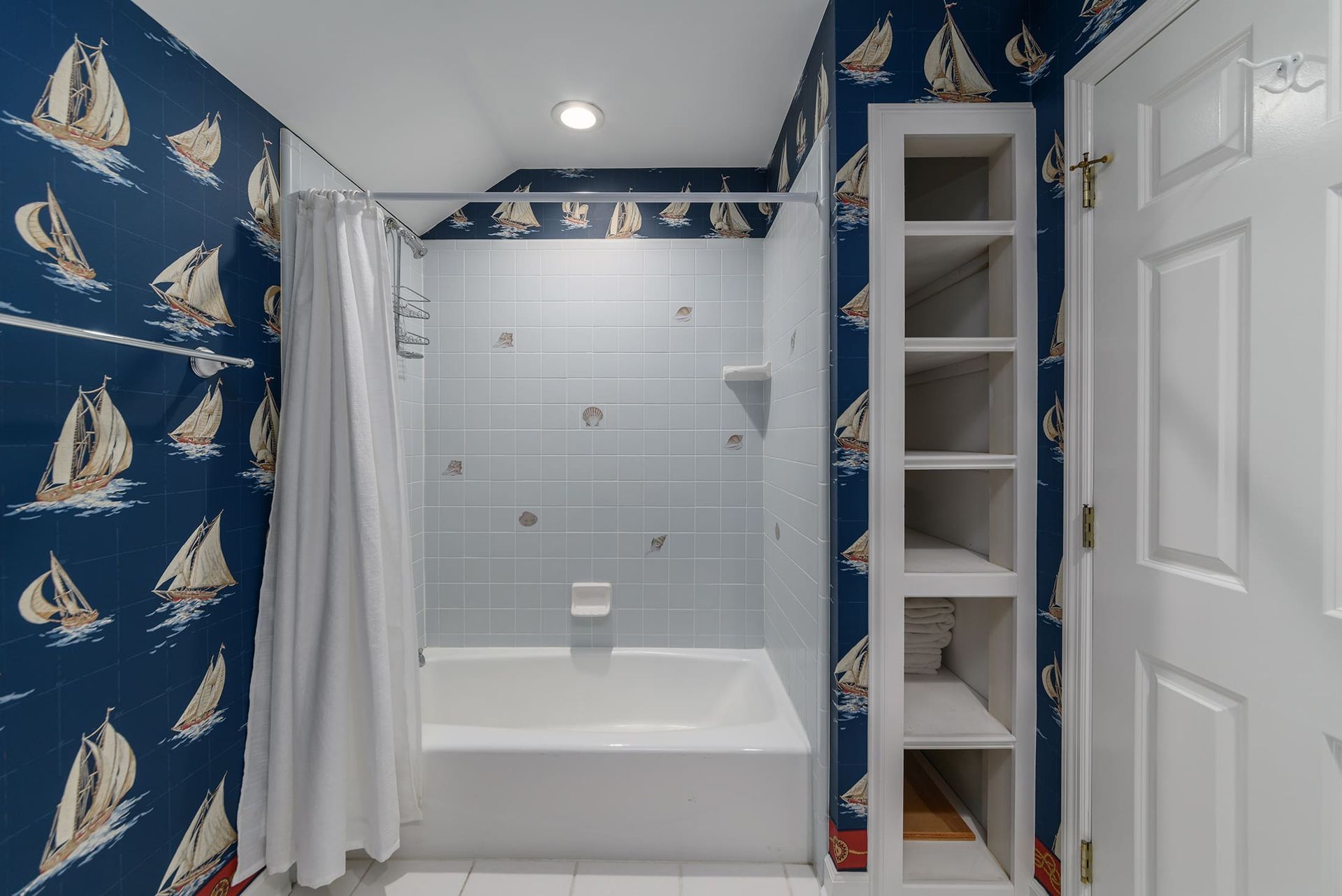 A bathroom with a bathtub and a shower with sailboats on the wall.