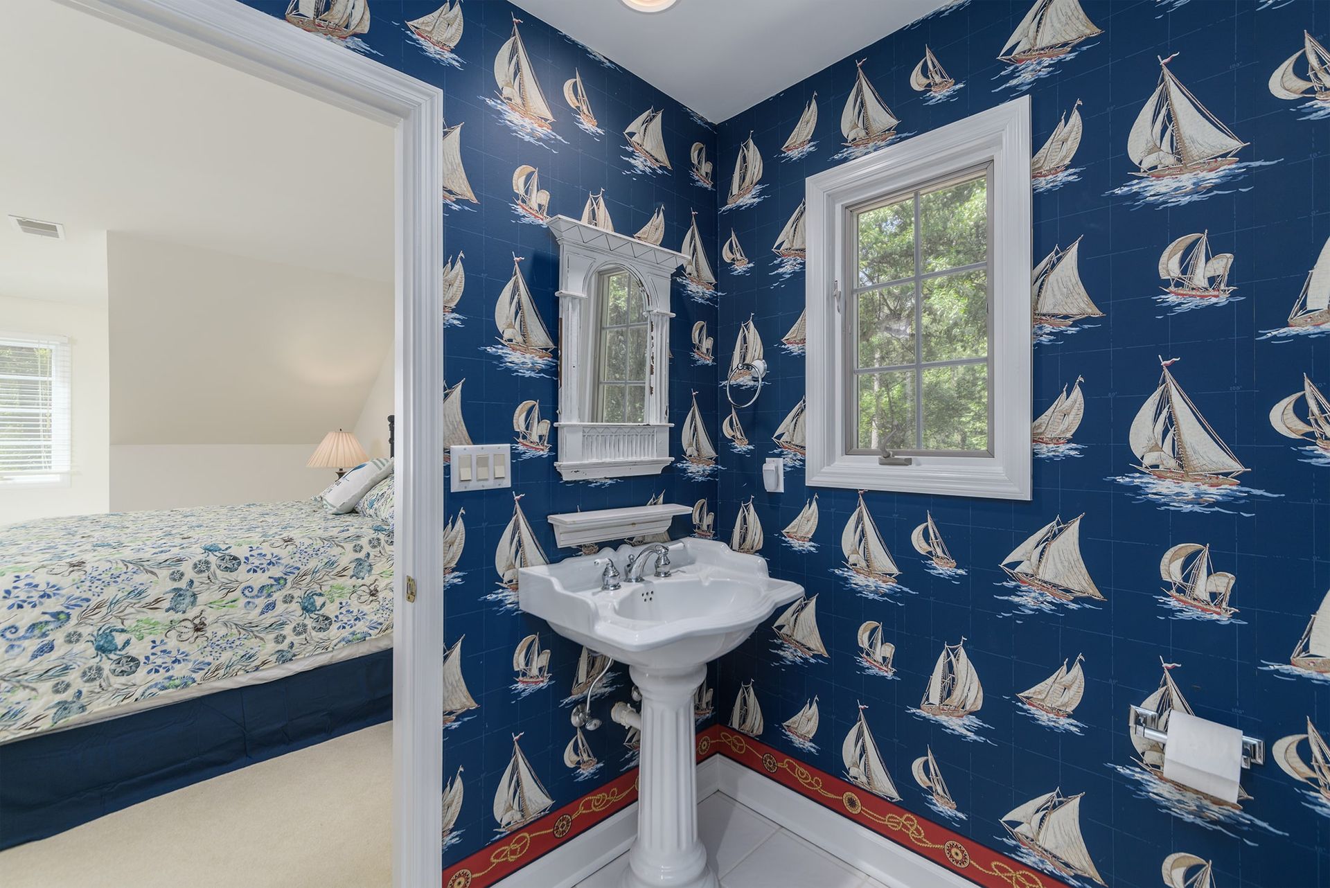A bathroom with a sink and a mirror with sailboats on the wall.