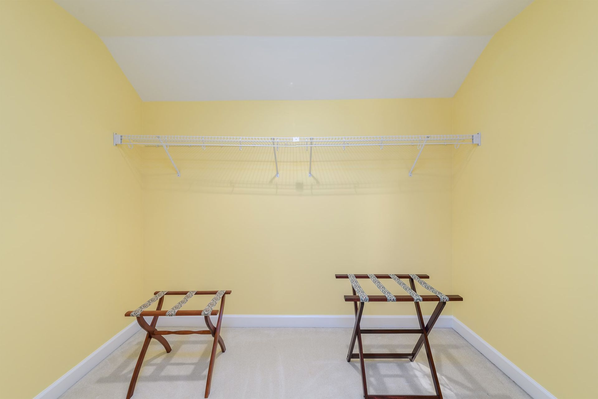 A closet with yellow walls and two luggage racks