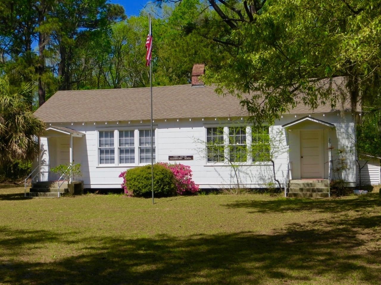 A small white house with a brown roof and a flag pole in front of it.