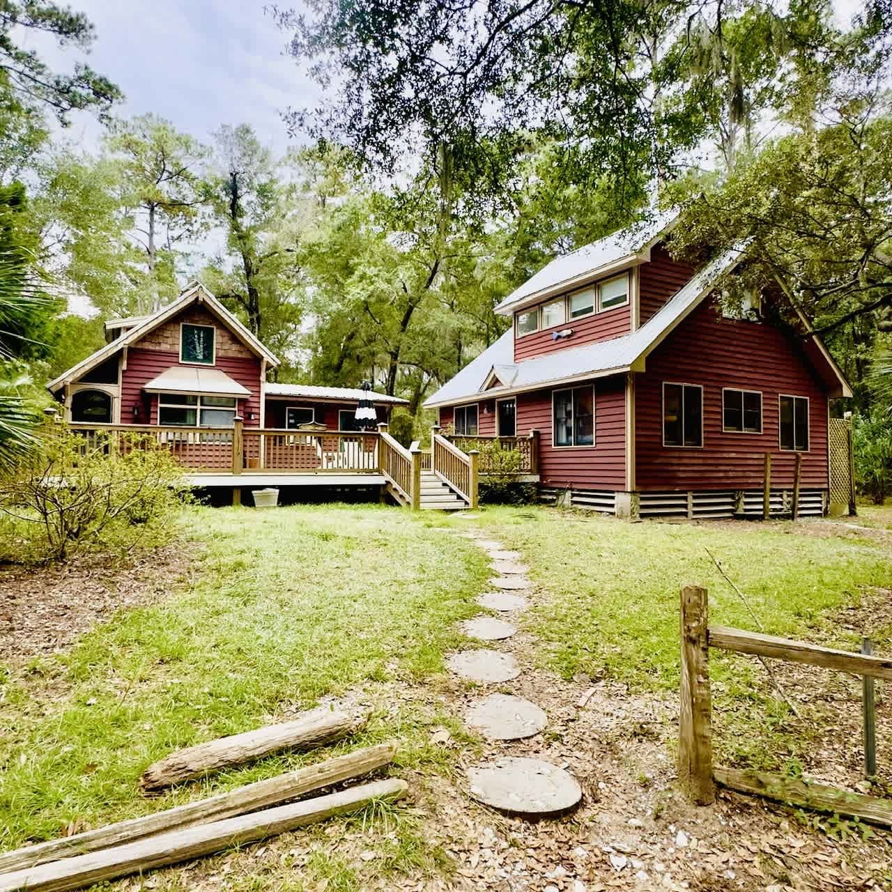 Two red wooden houses with a stone path in a green, wooded area.