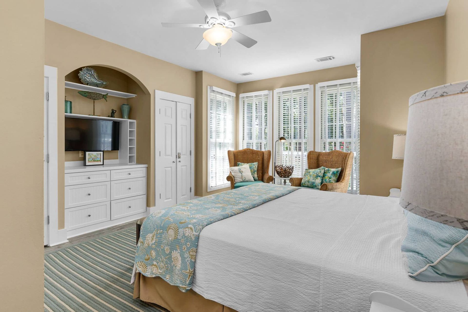 A bedroom with a king size bed , chairs , a television and a ceiling fan.