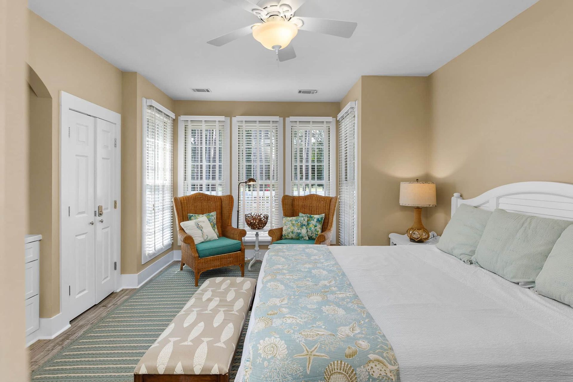 A bedroom with a king size bed , chair , bench and ceiling fan.