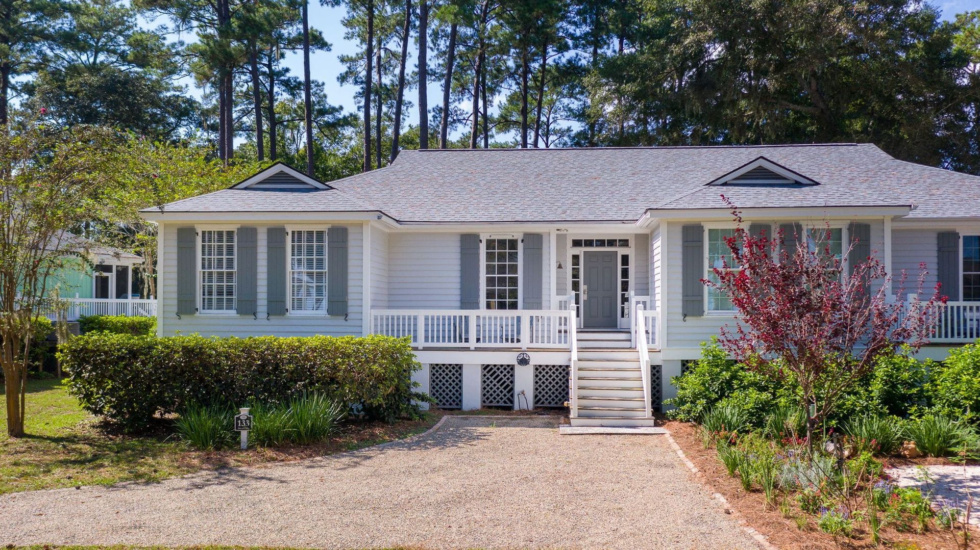 A white house with a gravel driveway and trees in the background.