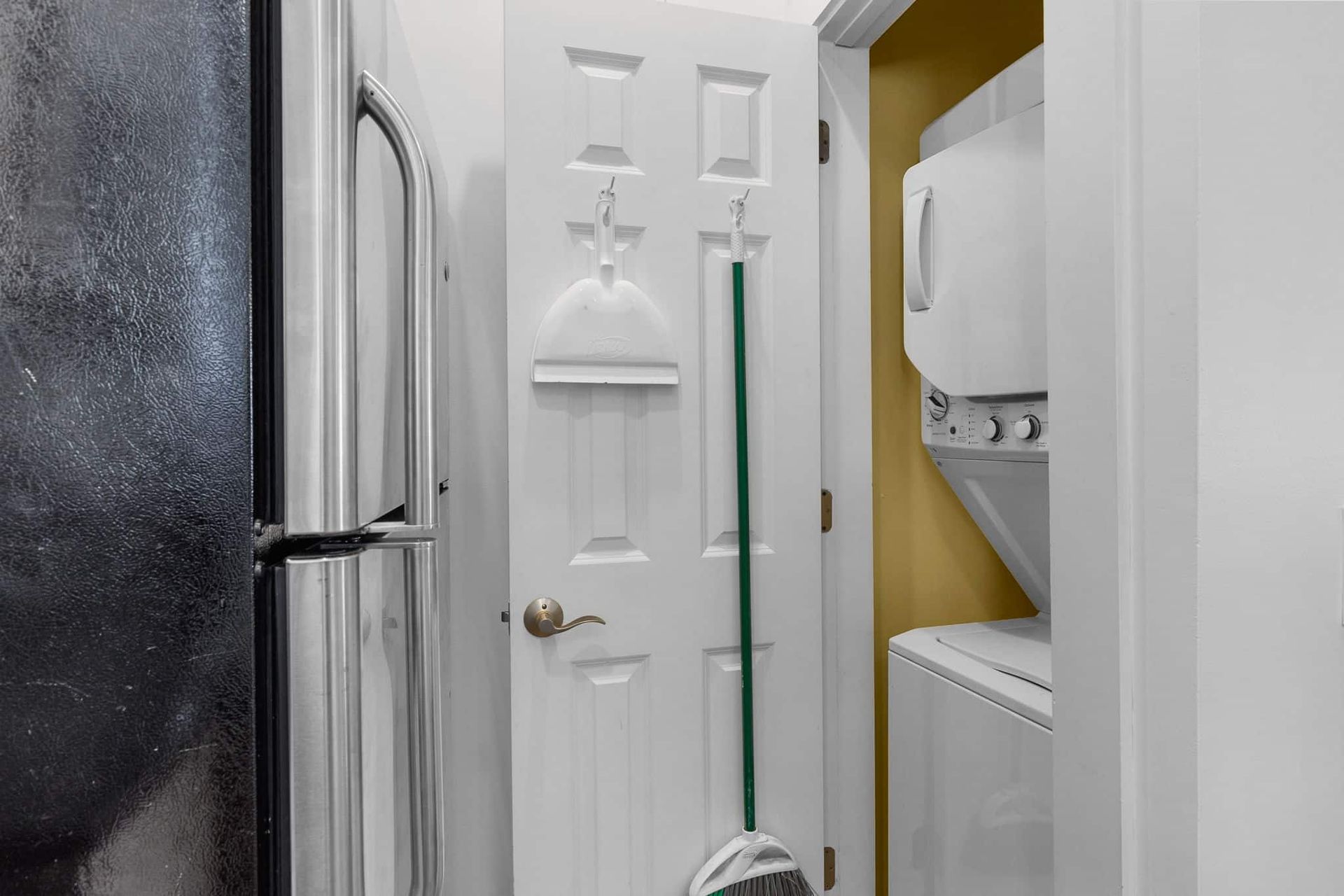 A laundry room with a refrigerator , washer and dryer and a mop.
