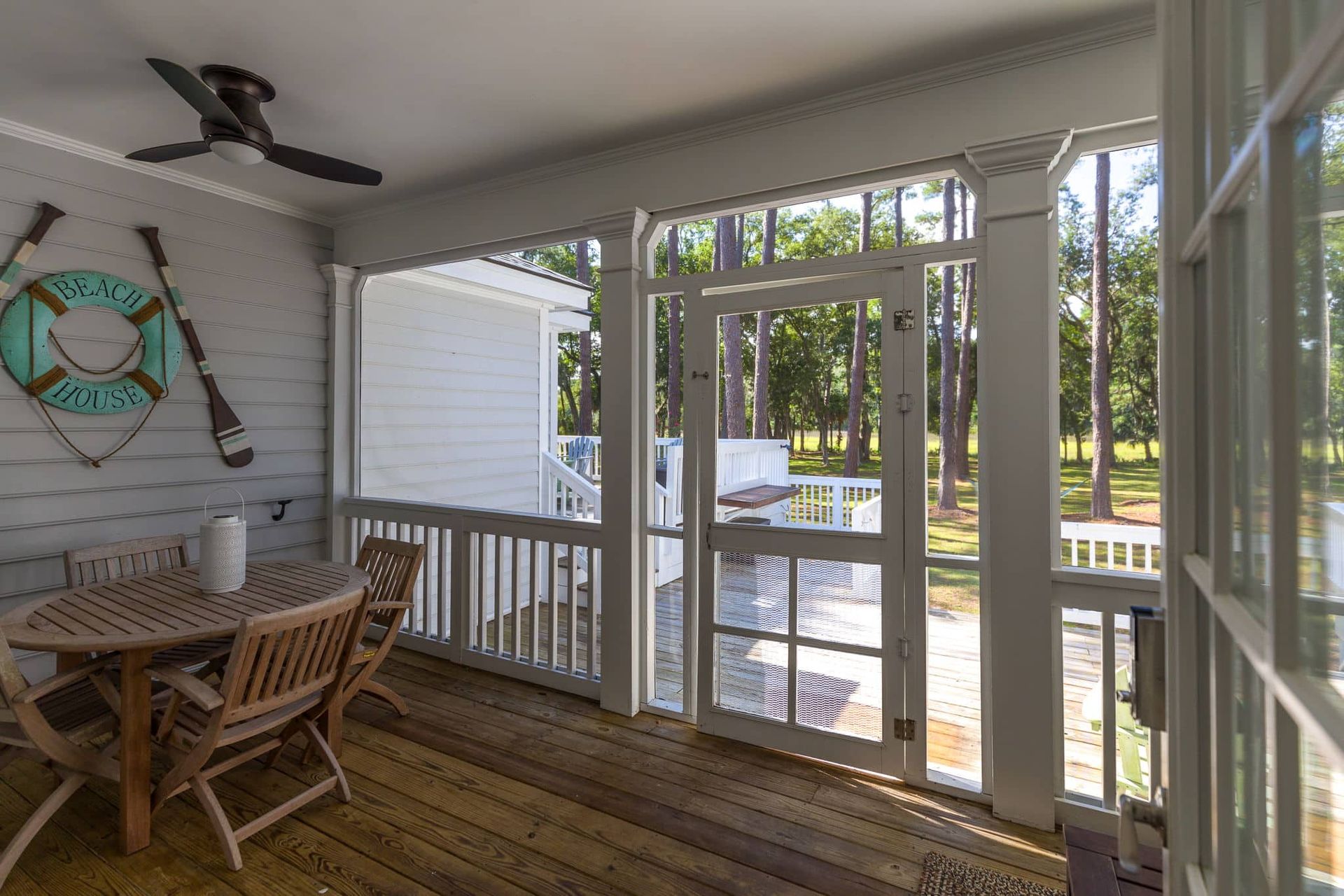 A screened in porch with a table and chairs and a ceiling fan.