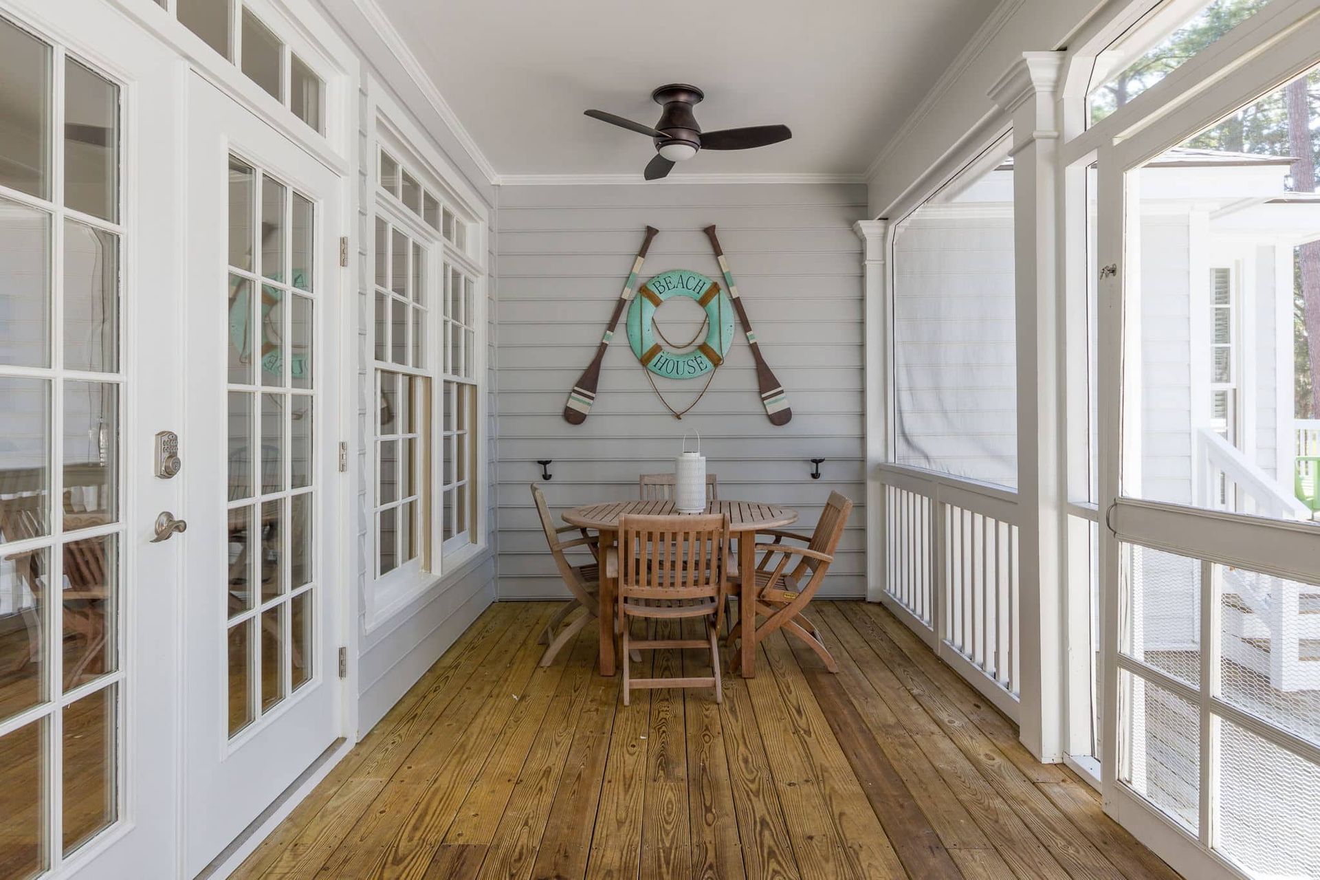 A screened in porch with a table and chairs and a ceiling fan.