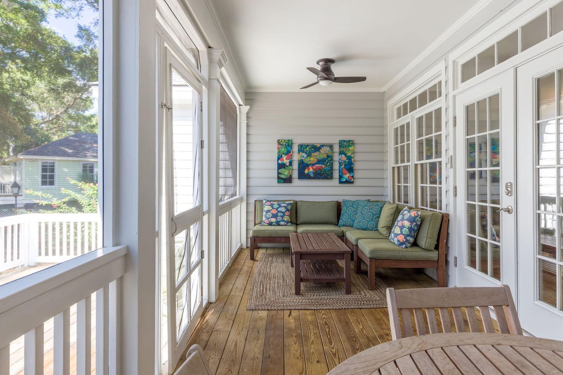 A screened in porch with a table and chairs and a ceiling fan.