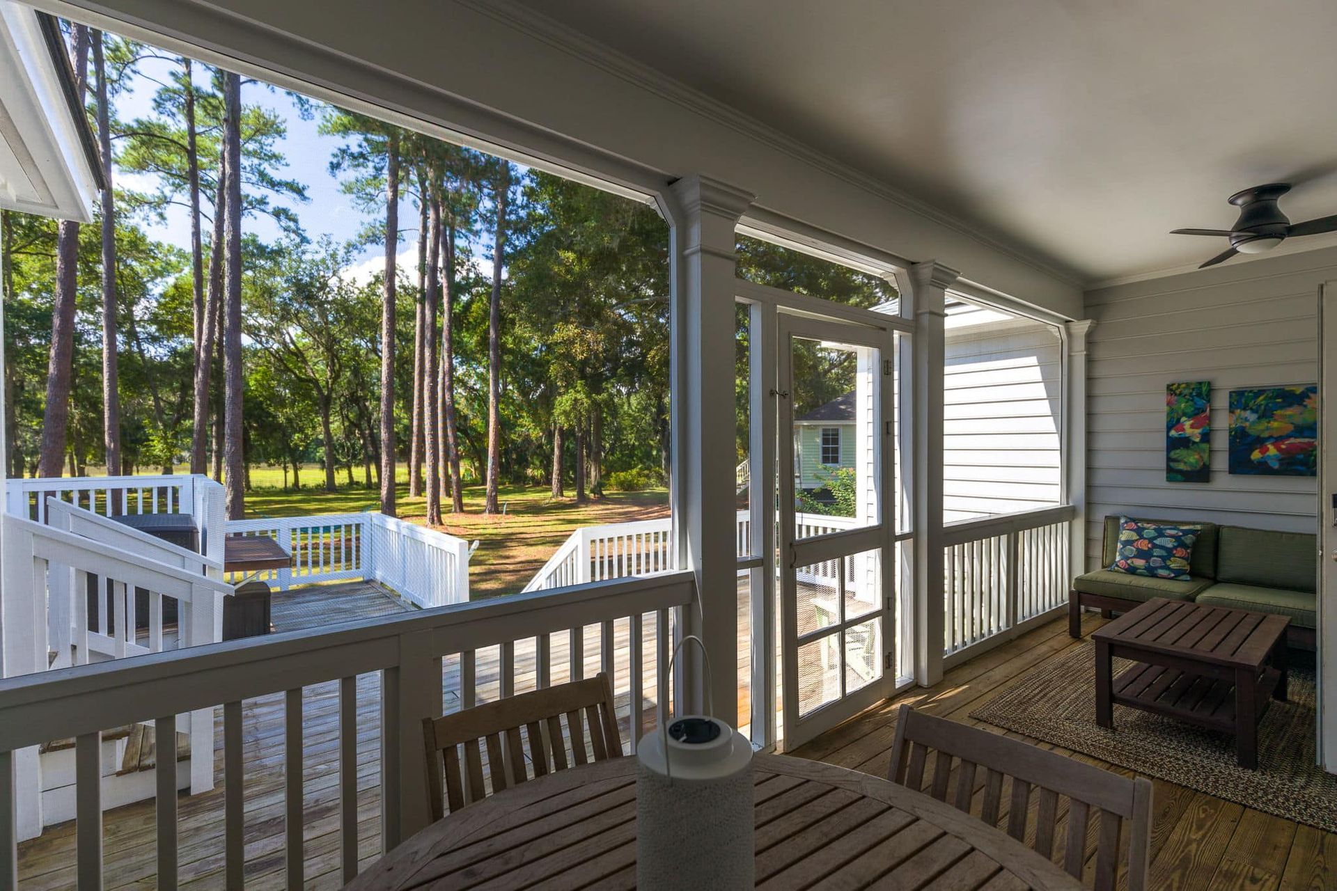 A screened in porch with a table and chairs and a ceiling fan.