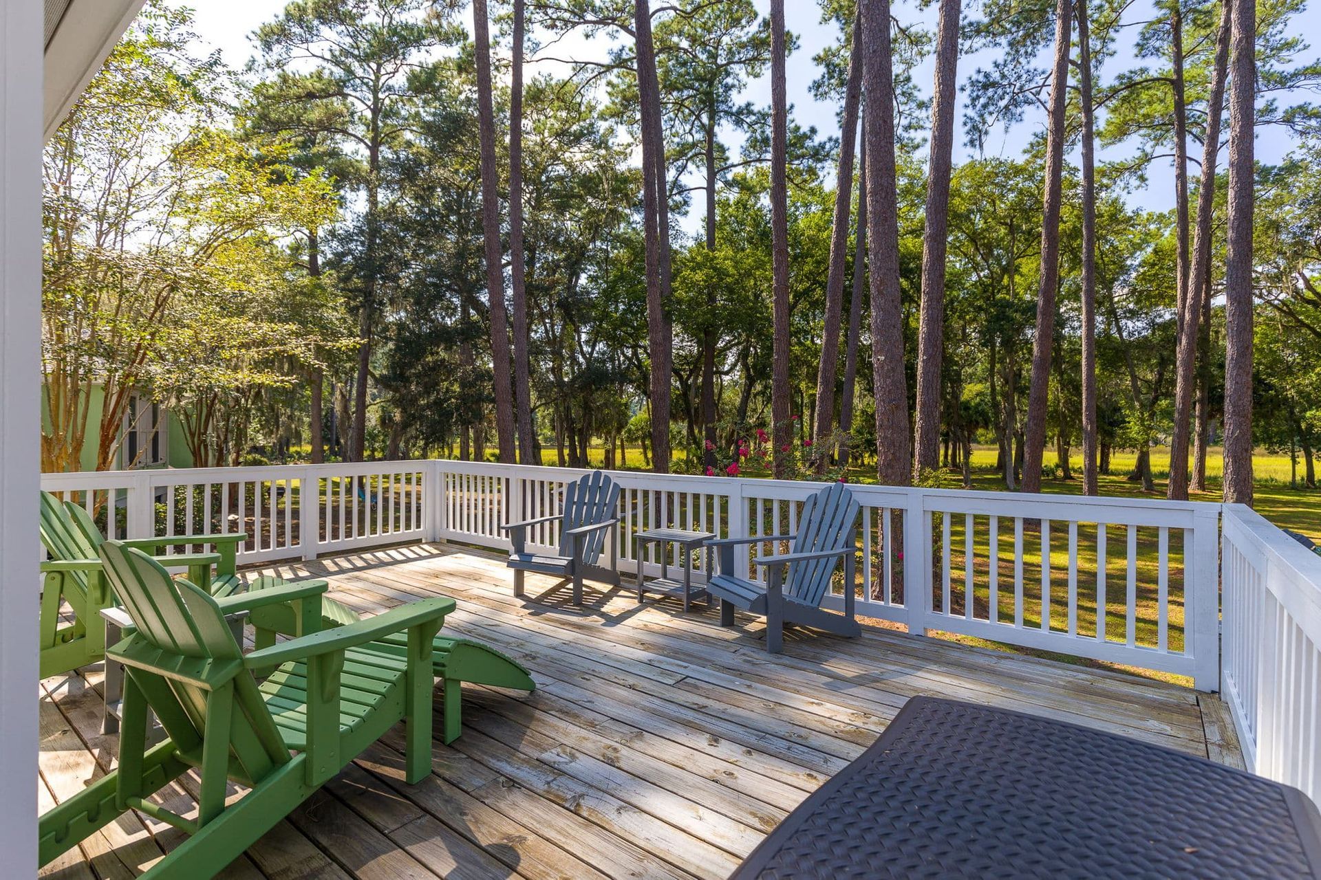A deck with green chairs and a white railing surrounded by trees.