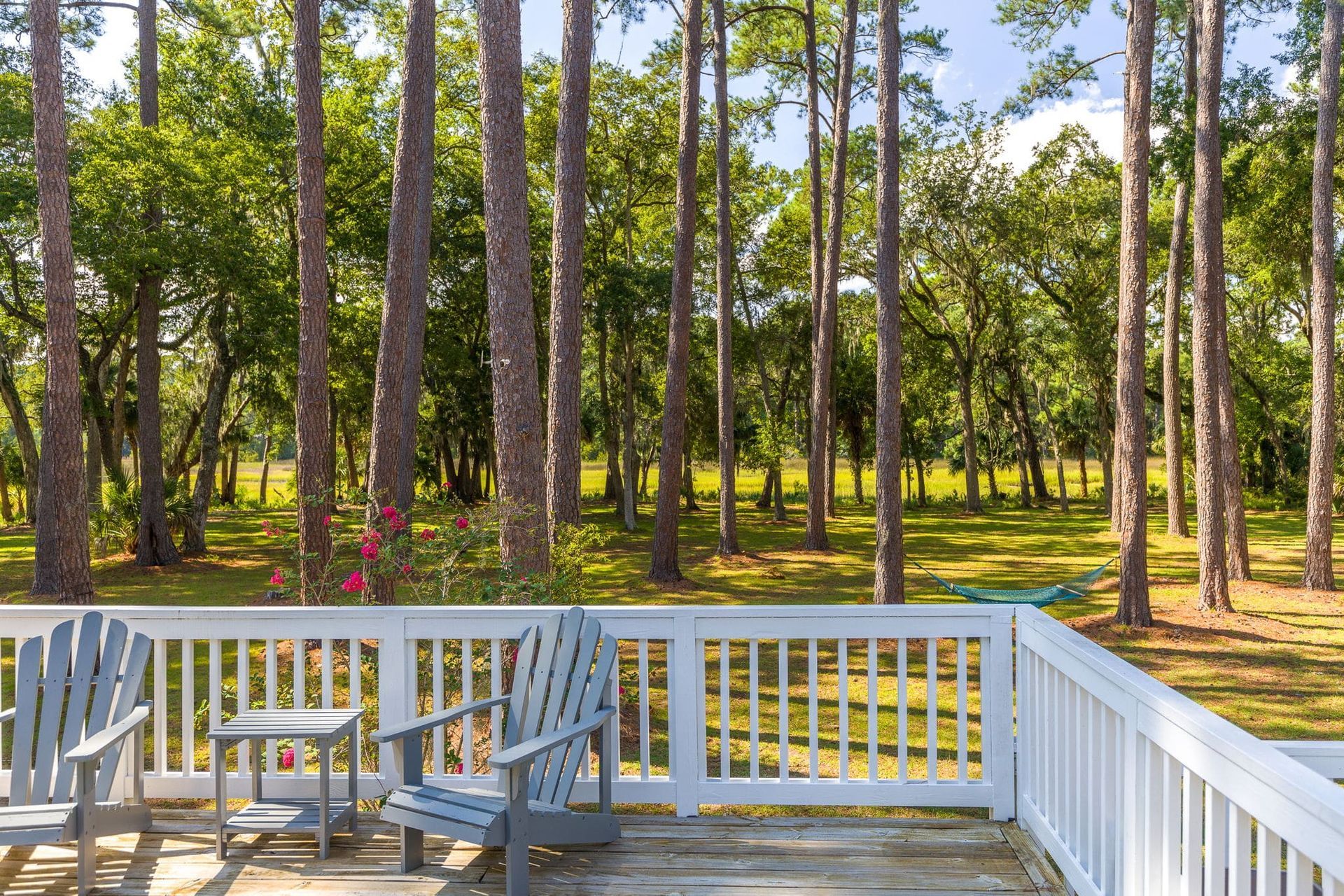 A deck with chairs and a table in front of a forest.