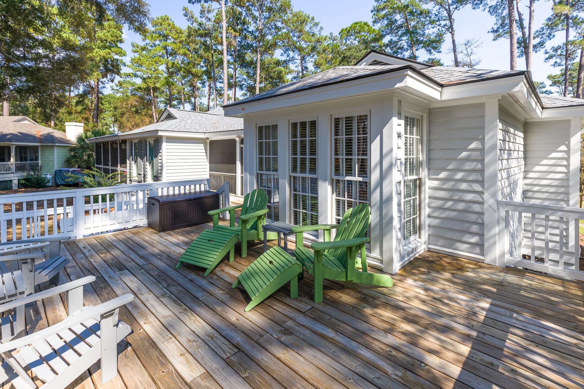 There are green chairs on the deck of a house.