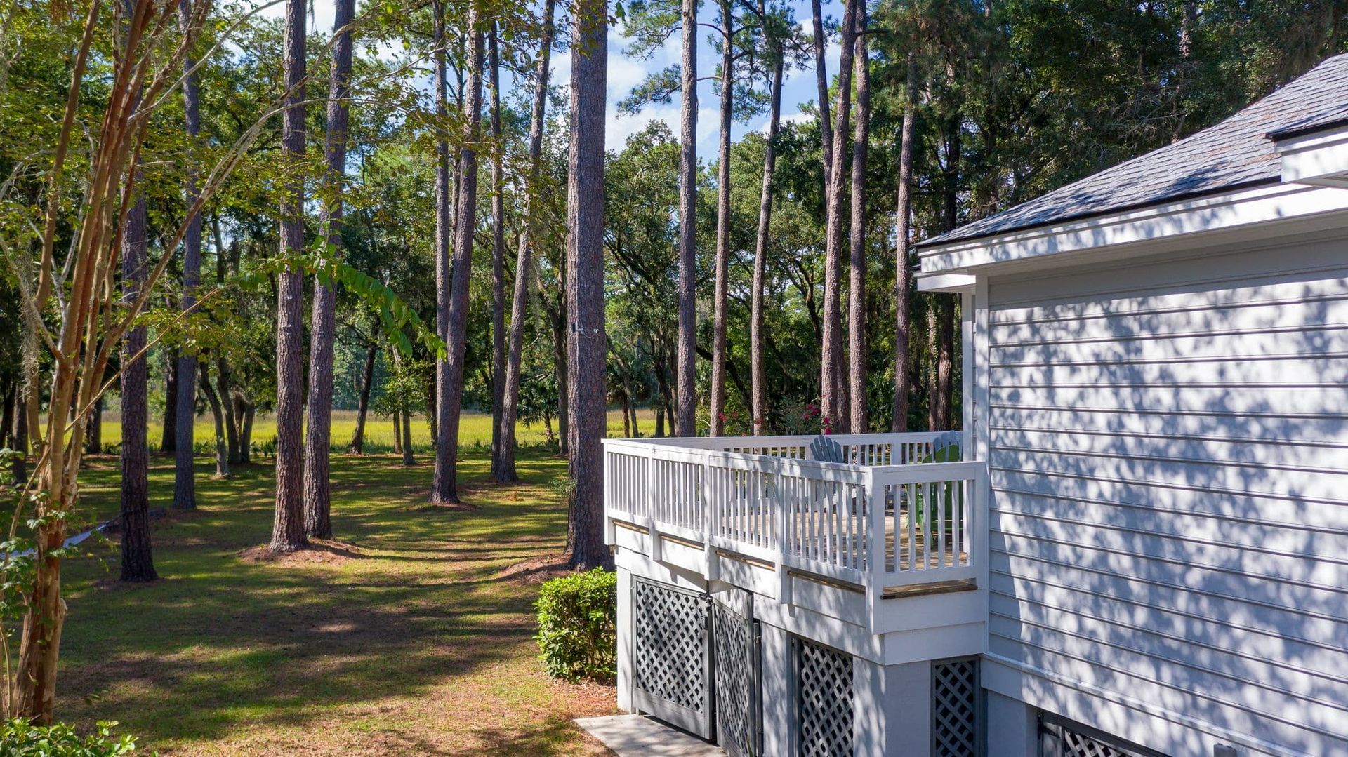 A white house with a large deck in the middle of a forest.