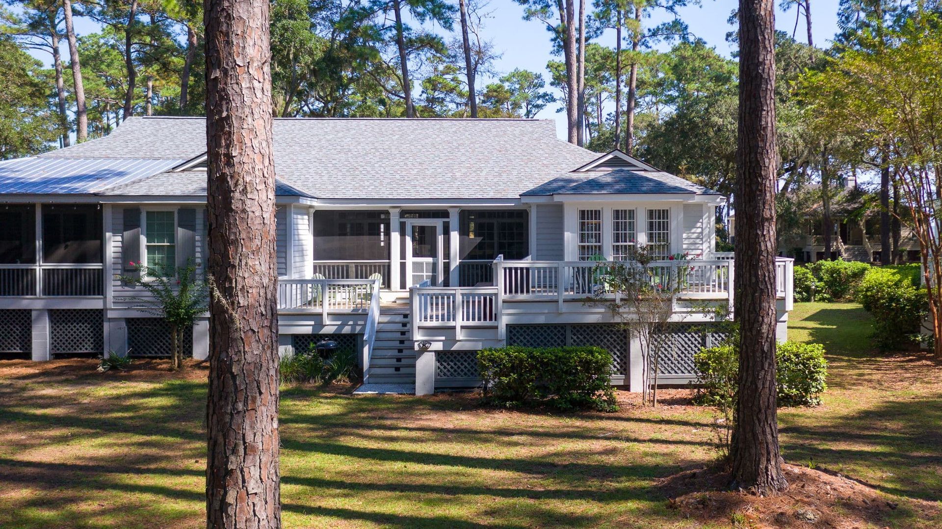A white house with a screened in porch is surrounded by trees.