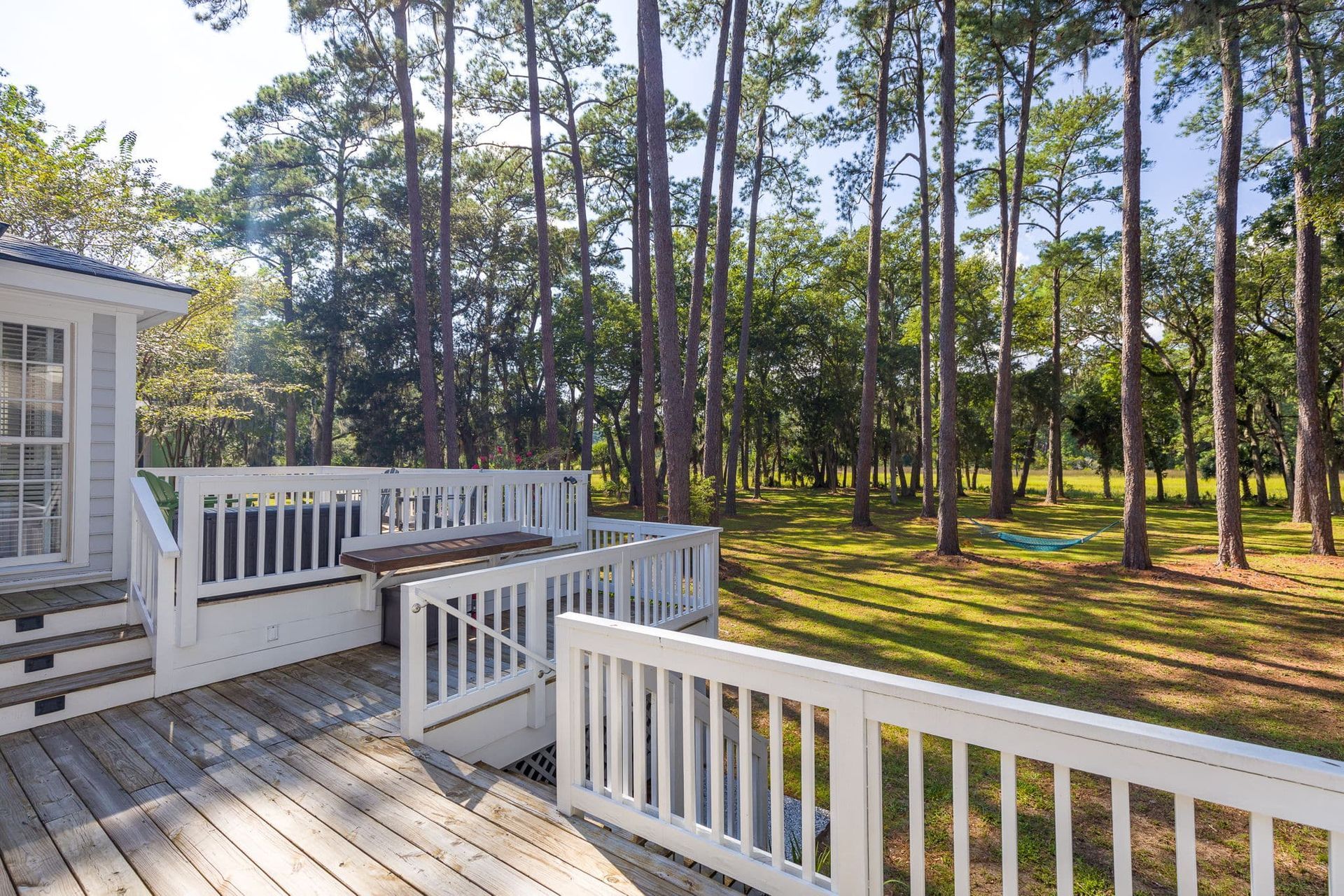 A small white house with a wooden deck in the middle of a forest.