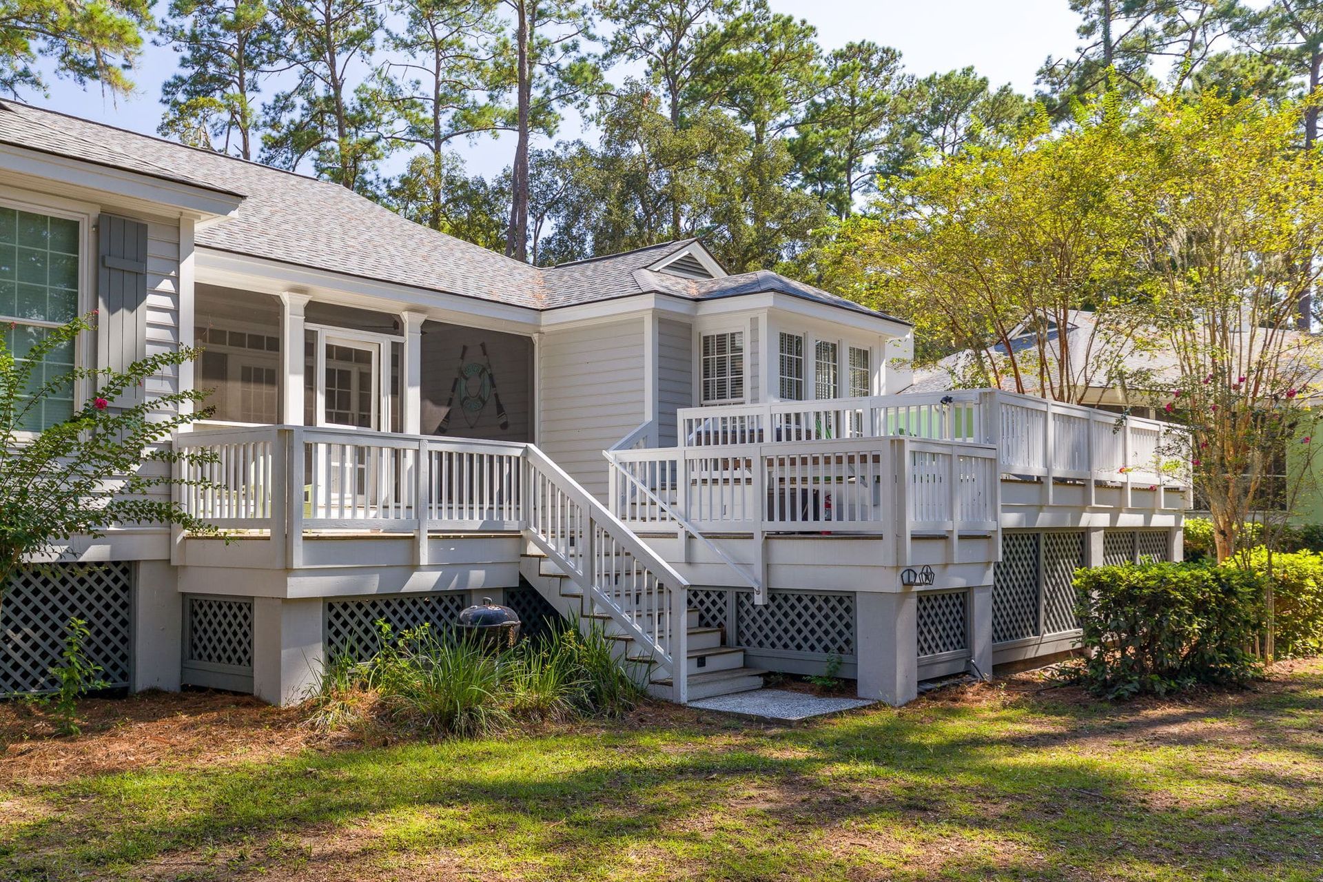 A white house with a large deck and stairs is surrounded by trees.