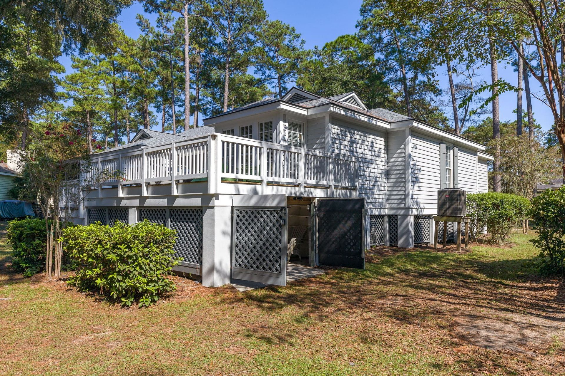 A white house with a large deck is surrounded by trees.