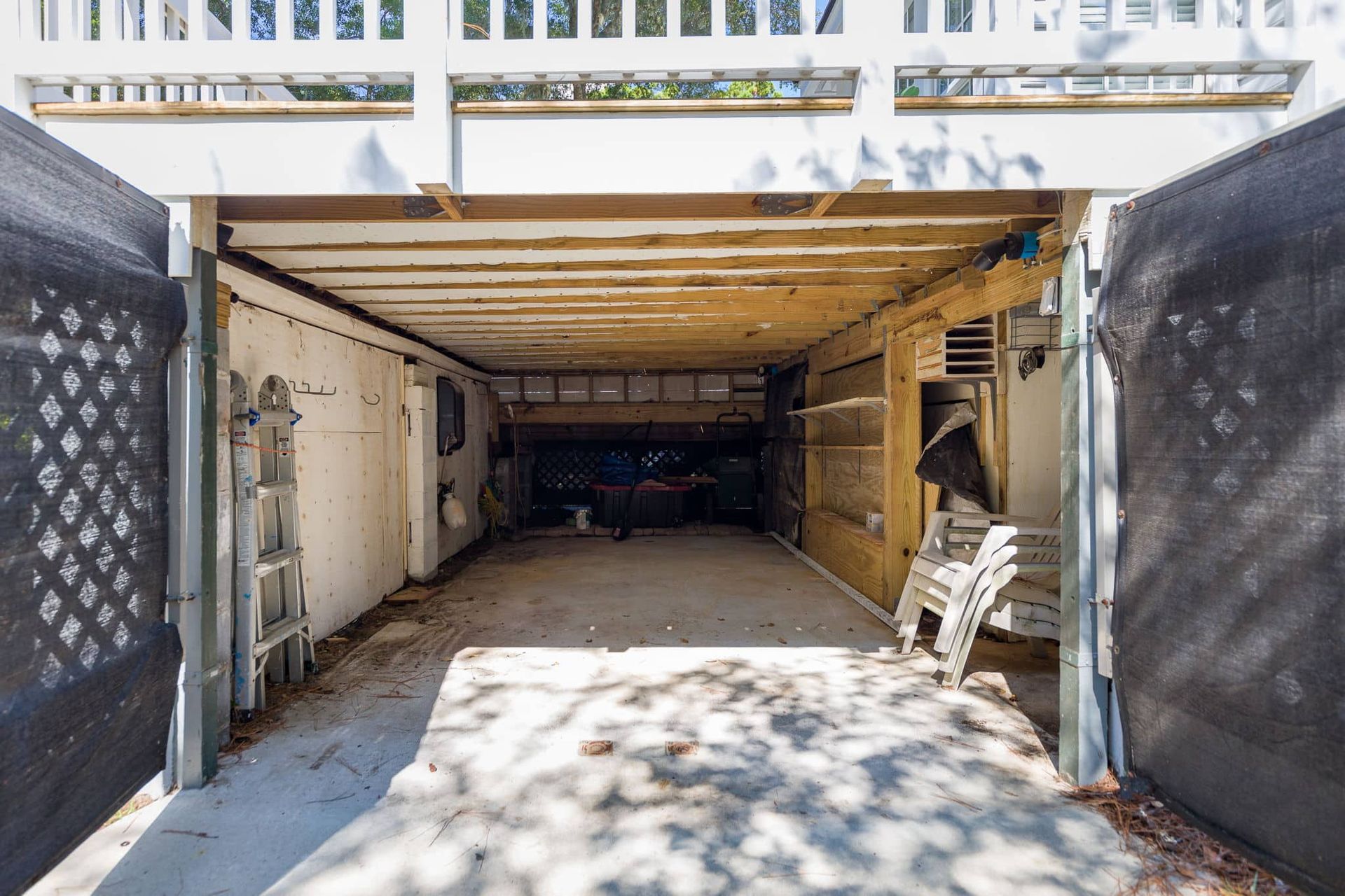 An empty garage with a ladder and chairs in it.