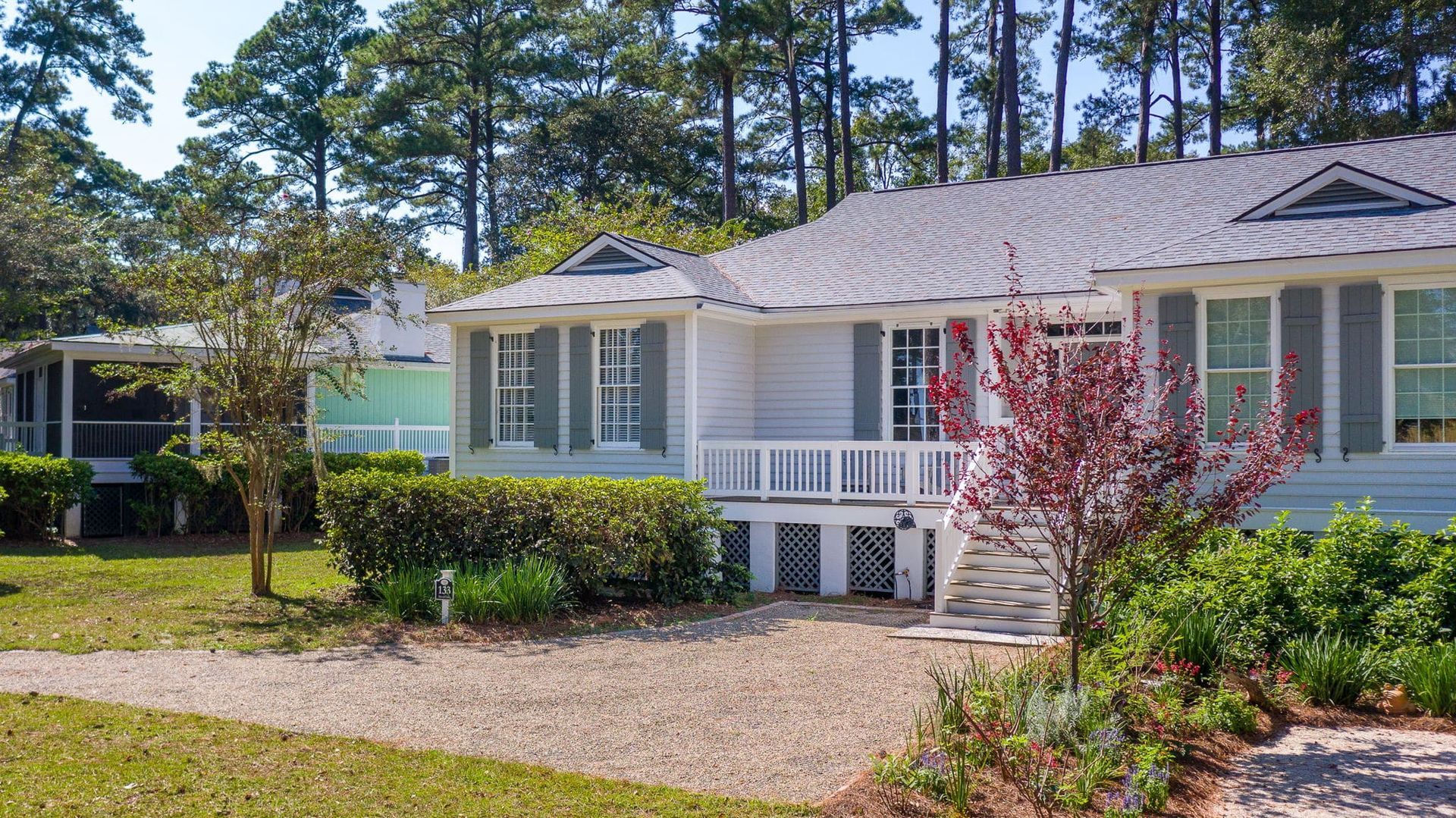 A white house with a gray roof and a green porch is surrounded by trees.