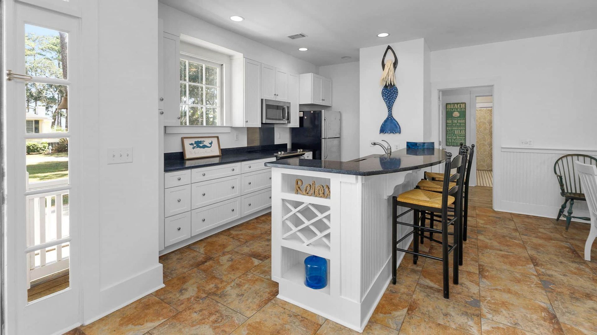 A kitchen with white cabinets , black counter tops , and a large island.