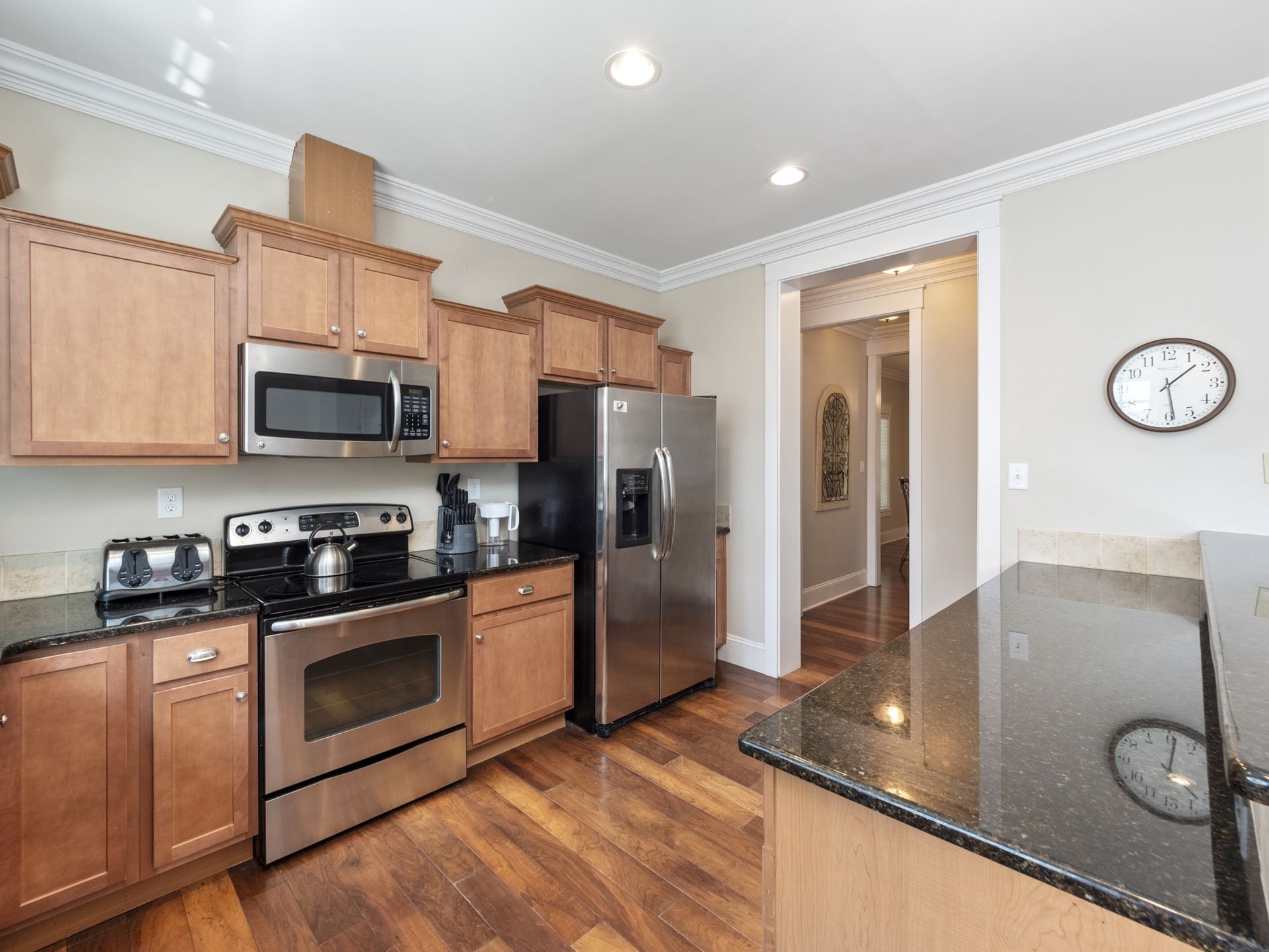 A kitchen with stainless steel appliances , wooden cabinets , granite counter tops and a clock on the wall.