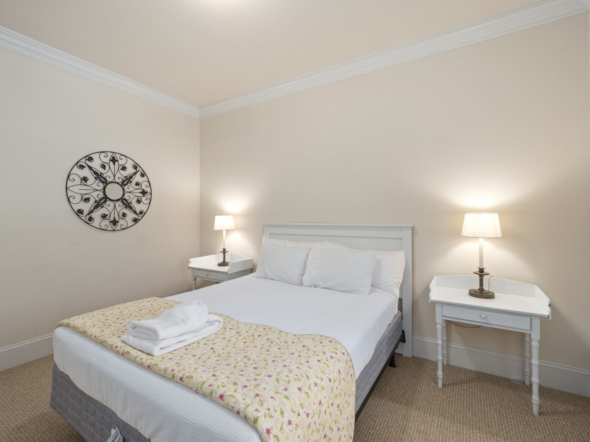 A bedroom with a bed , two nightstands and a clock on the wall.