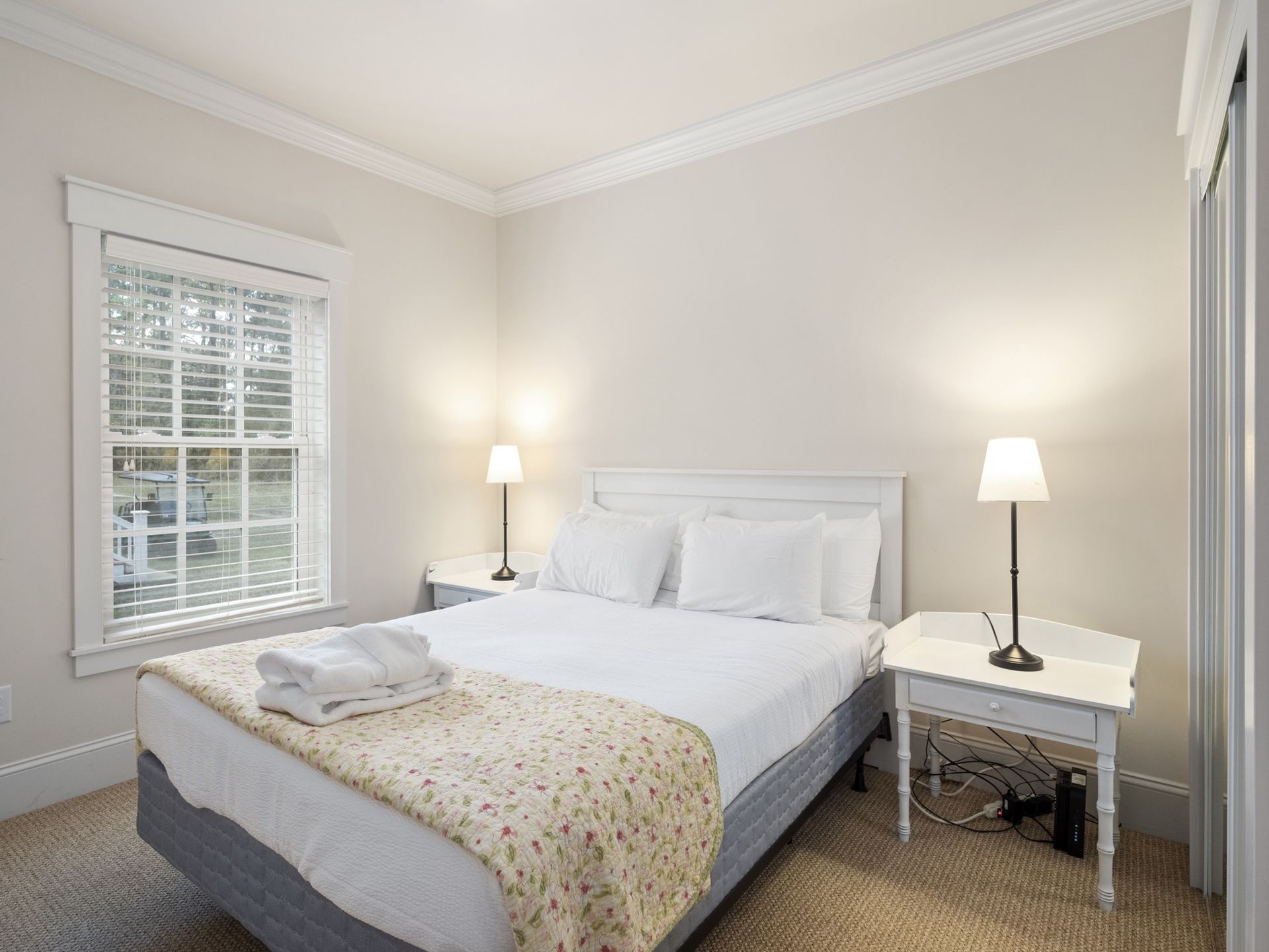 A bedroom with a bed , two nightstands , two lamps and a window.