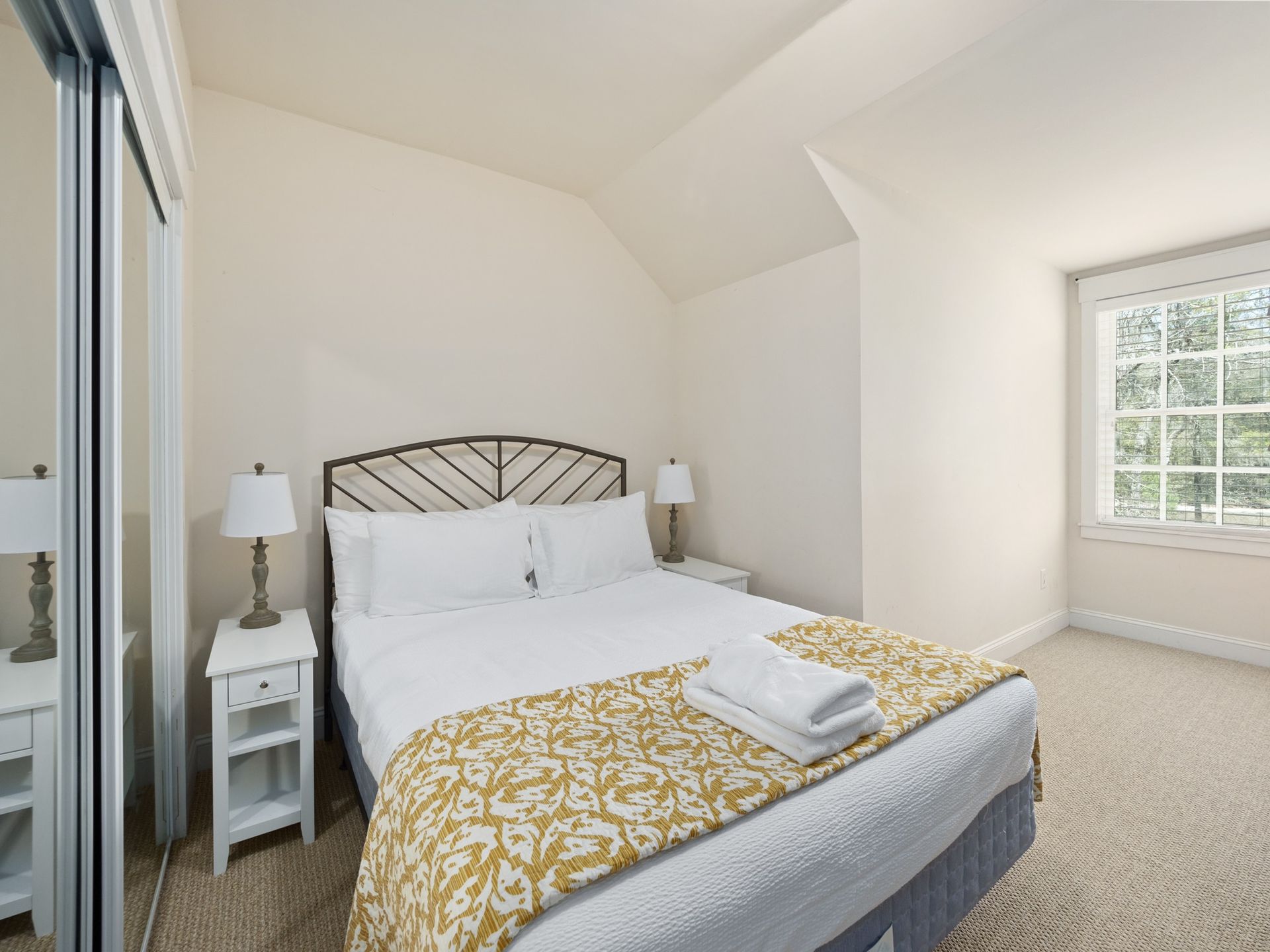 A bedroom with a bed , nightstands , lamps and a window.