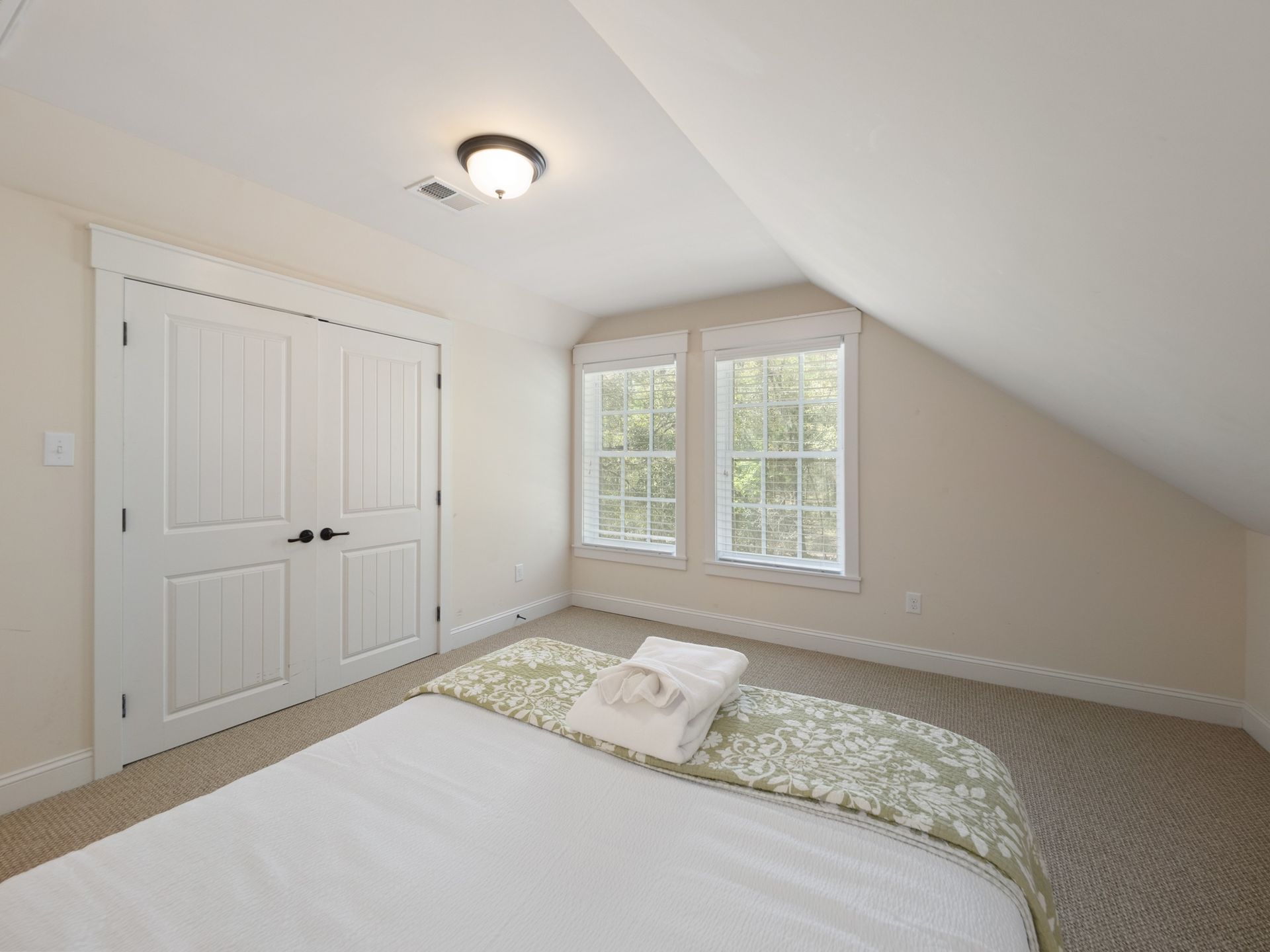 A bedroom with a bed , two windows and a closet.
