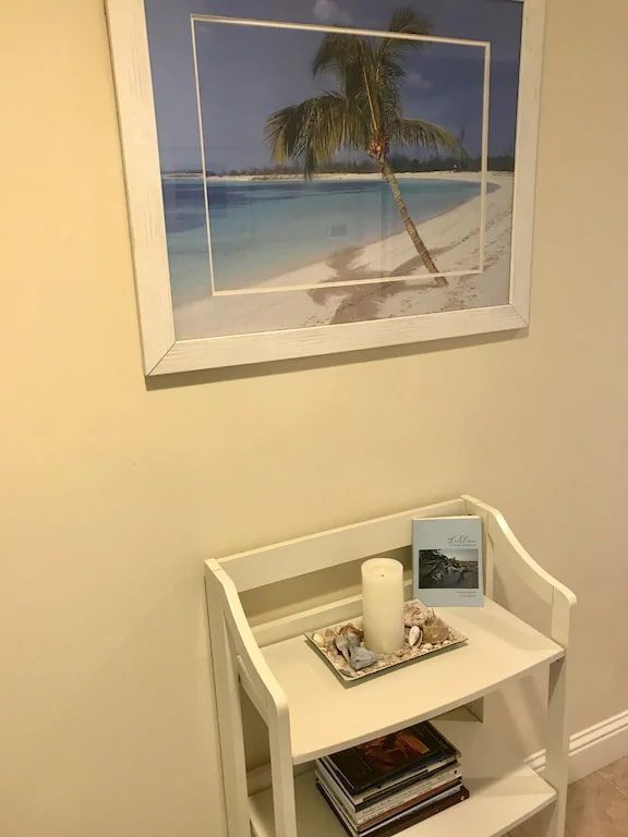 A picture of a beach is above a shelf with books and a candle on it