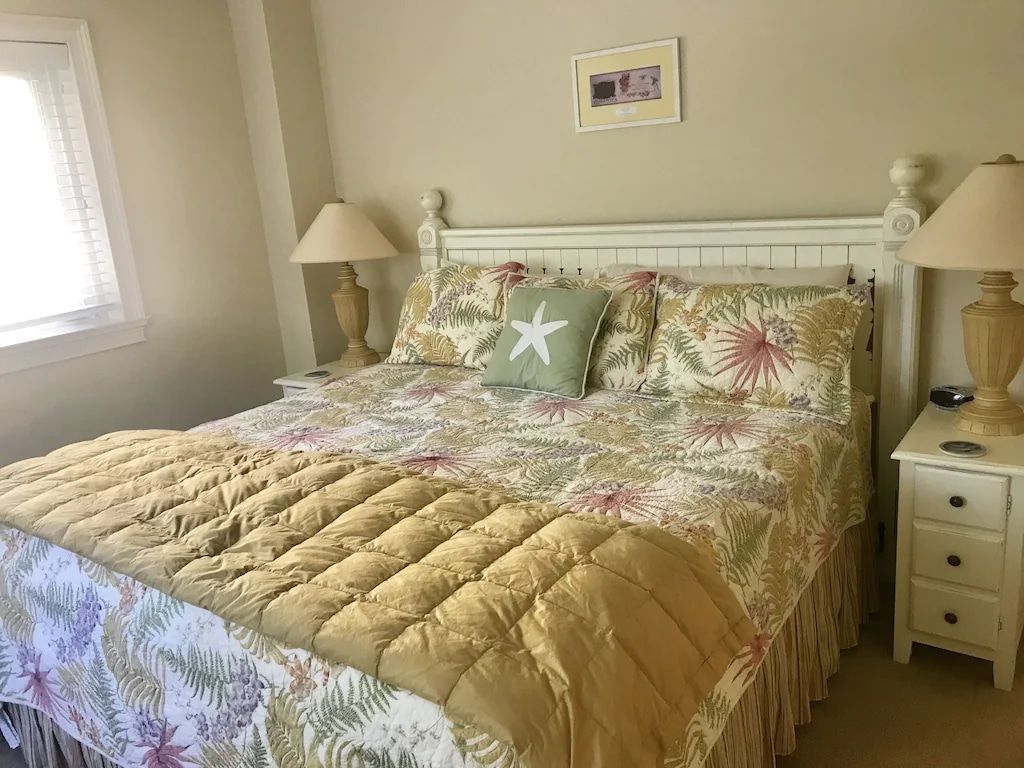 A bedroom with a king size bed , two lamps , a nightstand and a window.