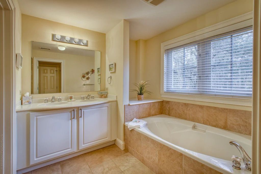 A bathroom with a tub , sink , mirror and window.