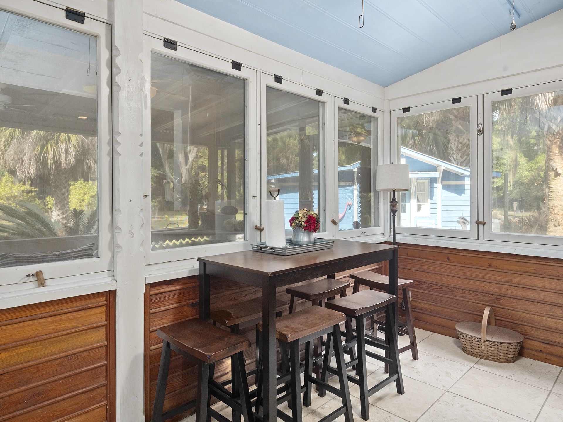 There is a table and stools in the room with a lot of windows.