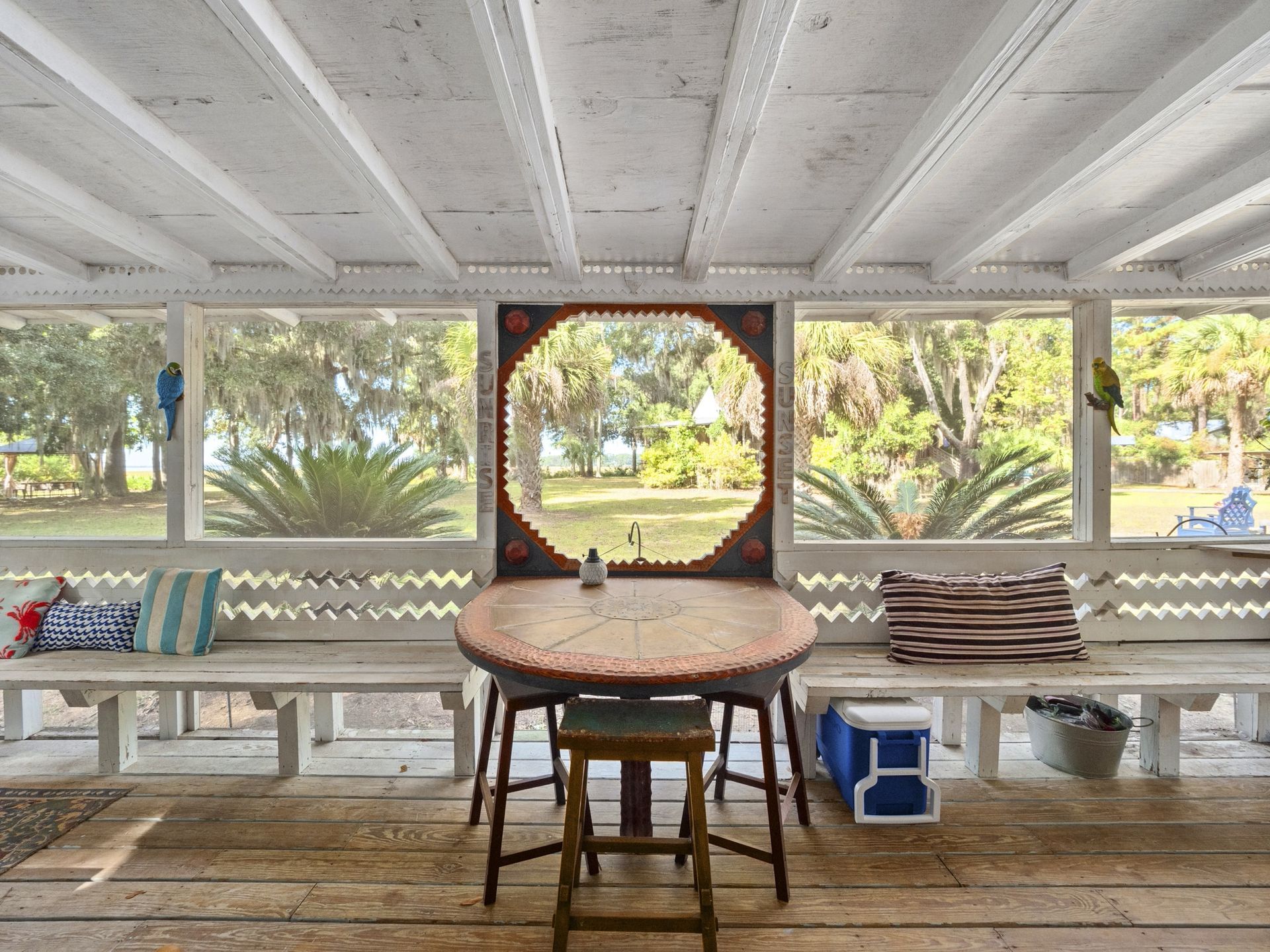 A screened in porch with a table and benches and a view of a lake.