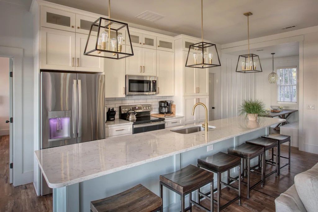 A kitchen with white cabinets , stainless steel appliances , a large island and stools.