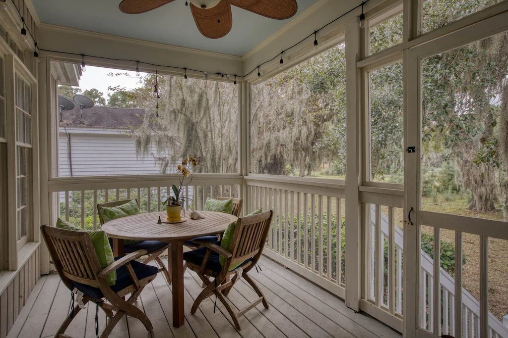 A screened in porch with a table and chairs and a ceiling fan.