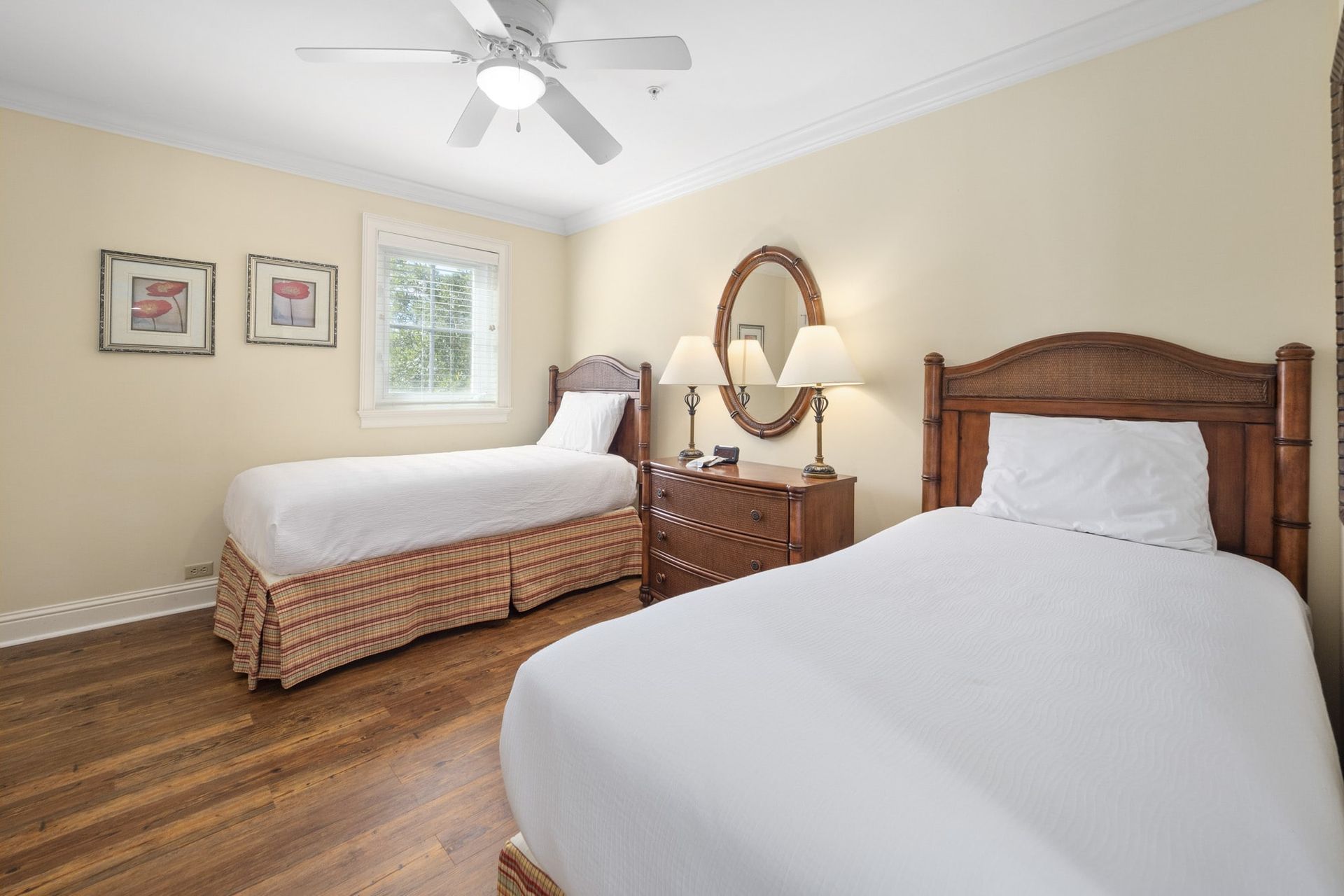 A bedroom with two beds , a dresser , a mirror and a ceiling fan.