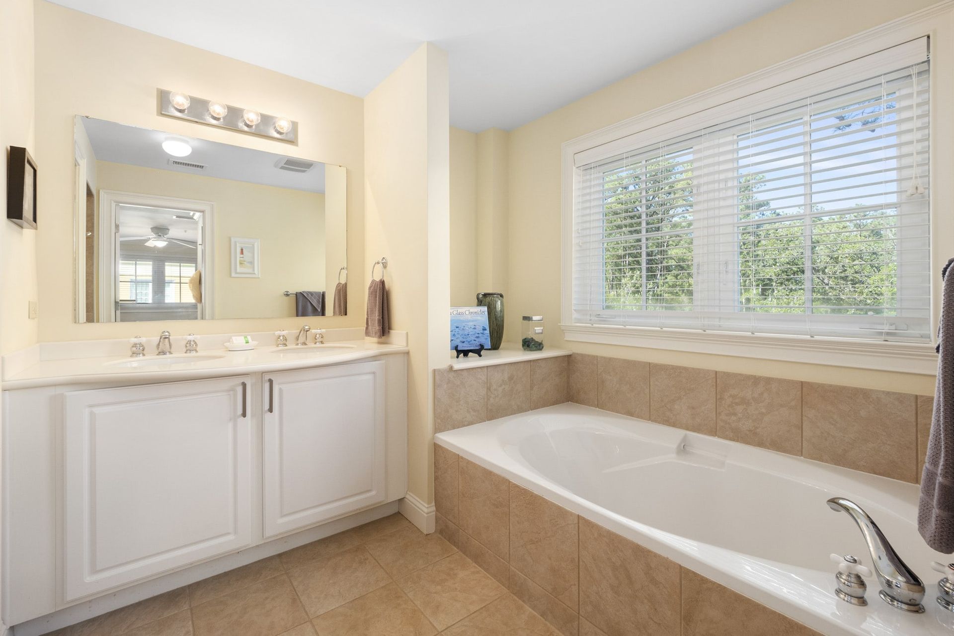 A bathroom with a tub , sink , mirror and window.
