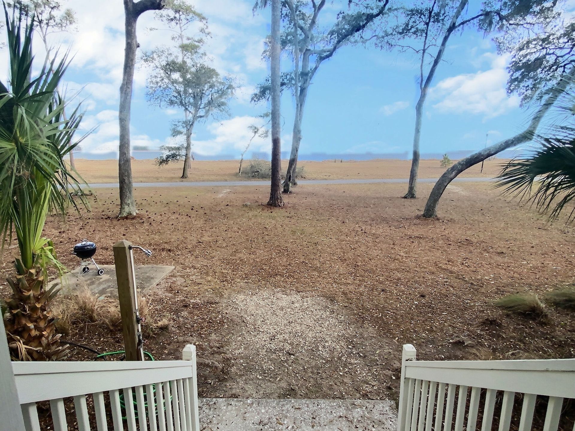 A view of a beach from a porch with trees in the background