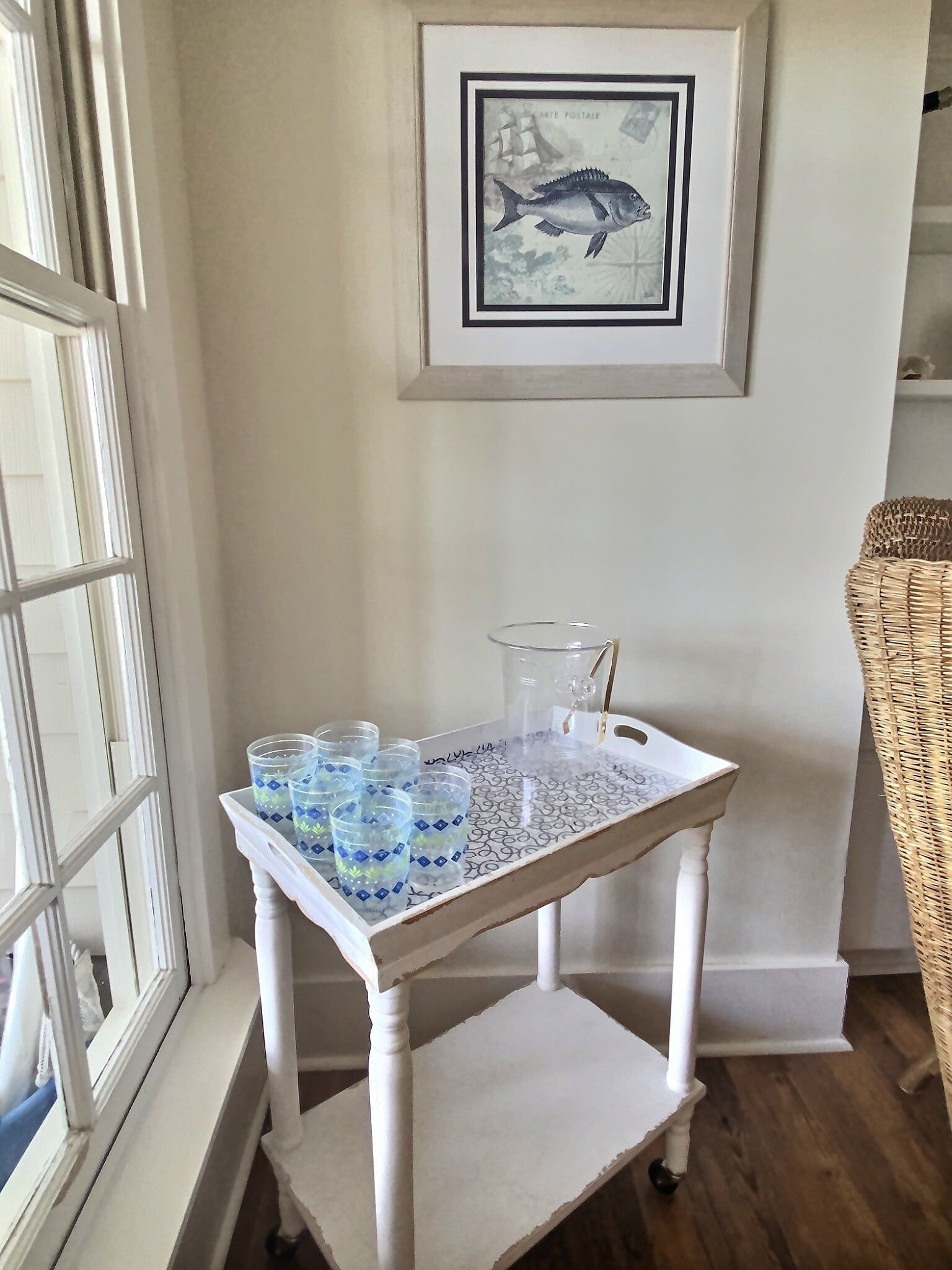 There is a picture of a fish on the wall above a tray with glasses on it.