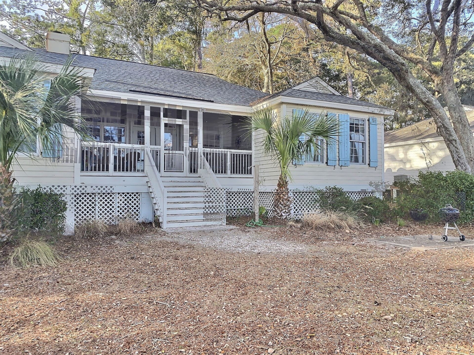 A white house with a large porch and palm trees in front of it.
