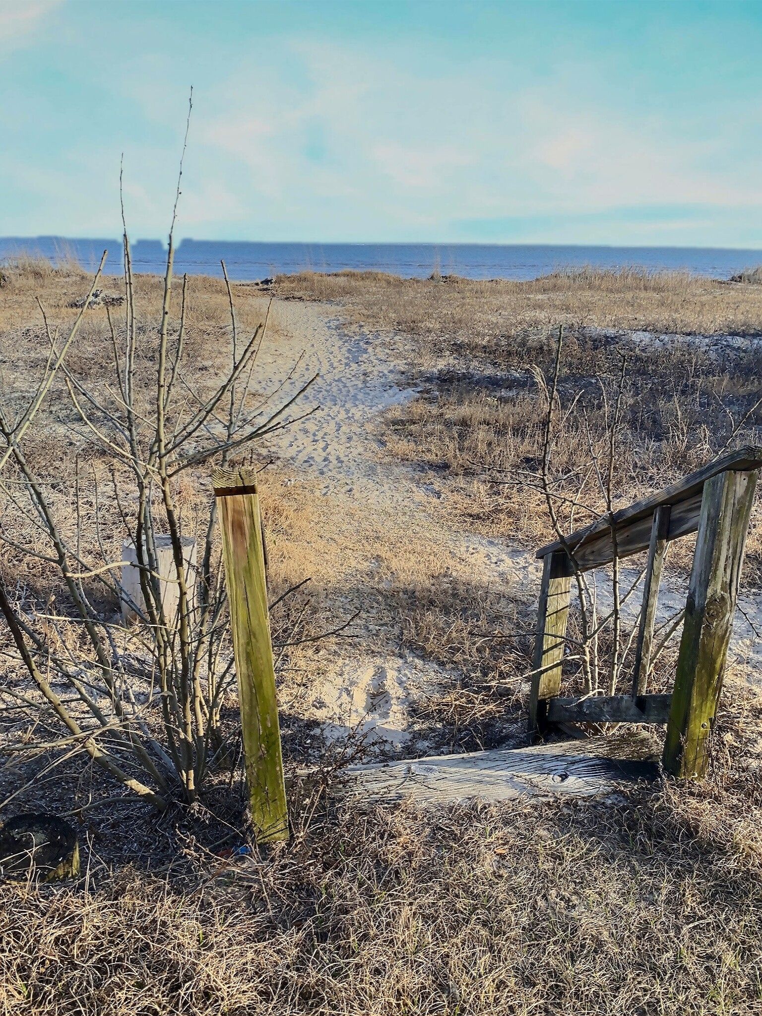 There is a wooden fence in the middle of a field leading to the ocean.