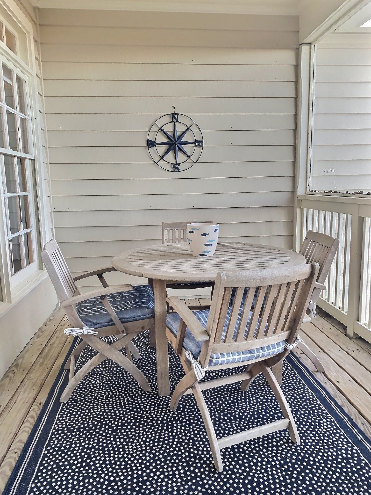 A porch with a table and chairs and a compass on the wall.