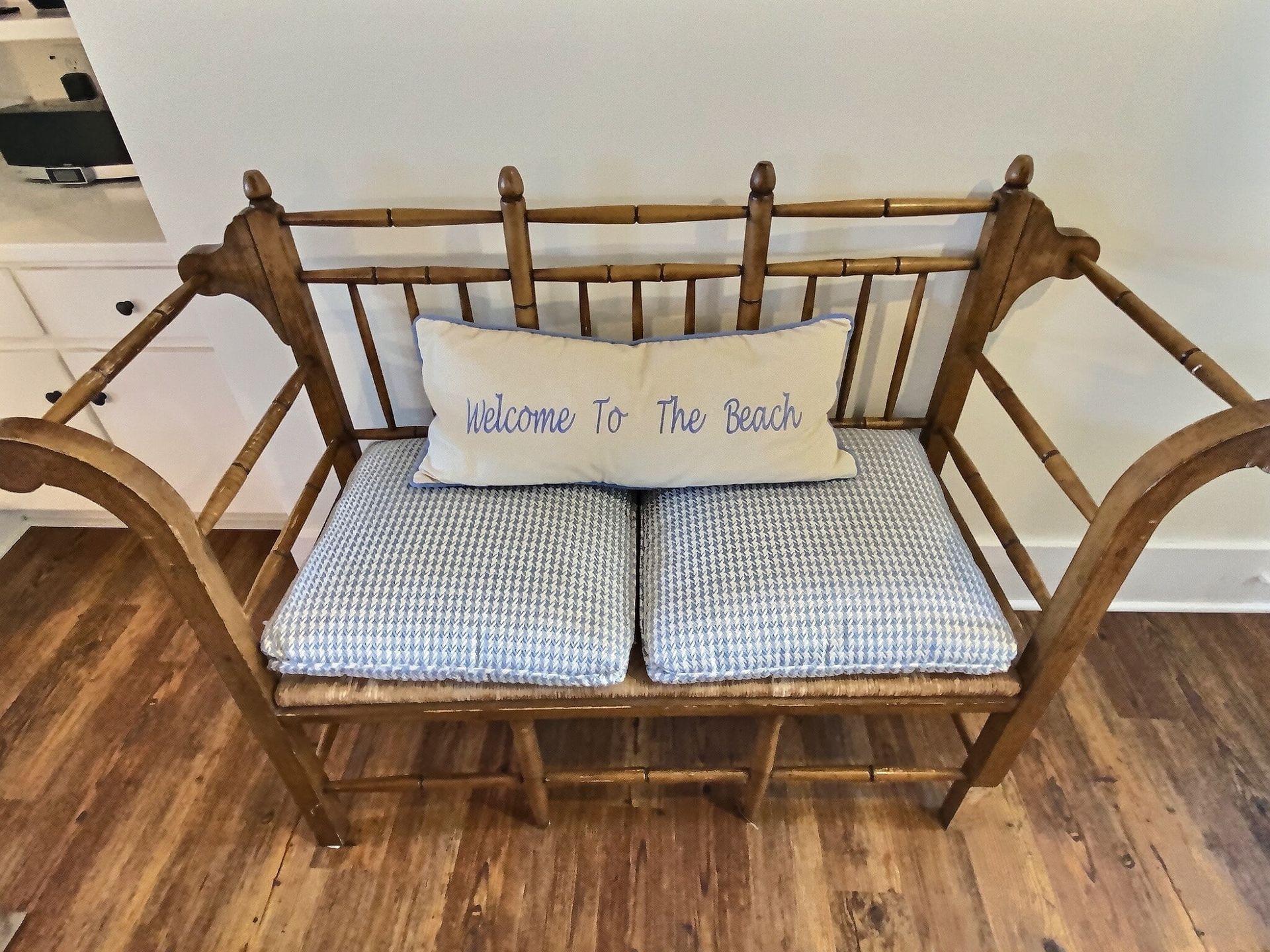 A wooden bench with a pillow that says welcome to the beach