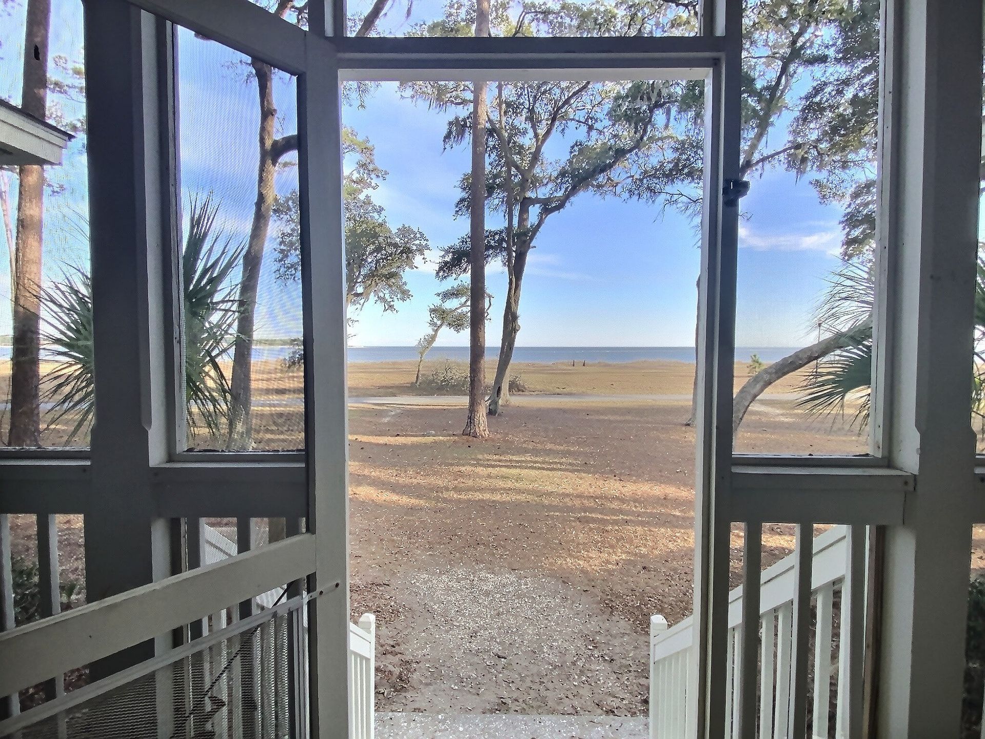 A screened in porch with a view of the ocean and trees.