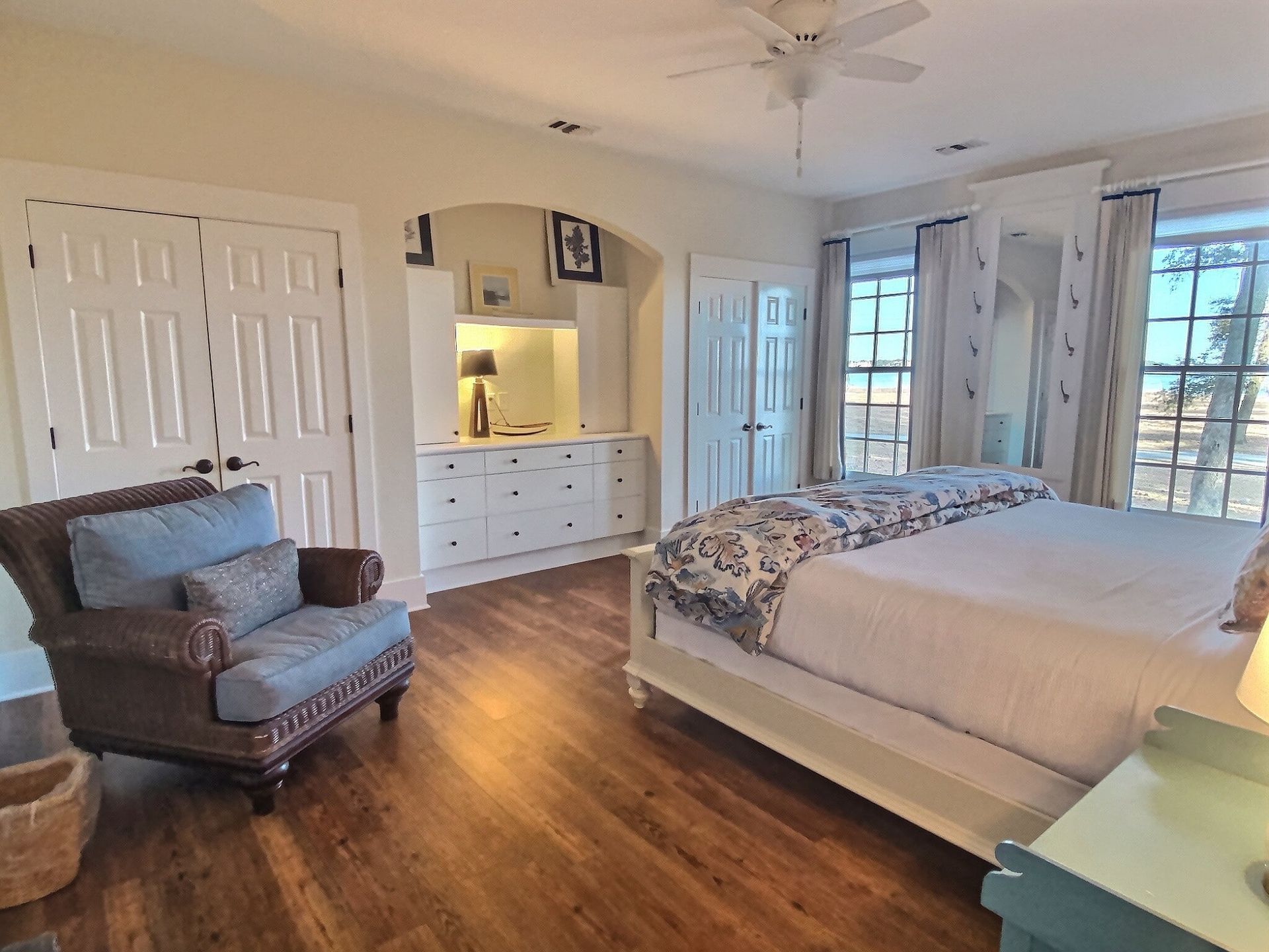 A bedroom with a king size bed , chair , nightstand and ceiling fan.