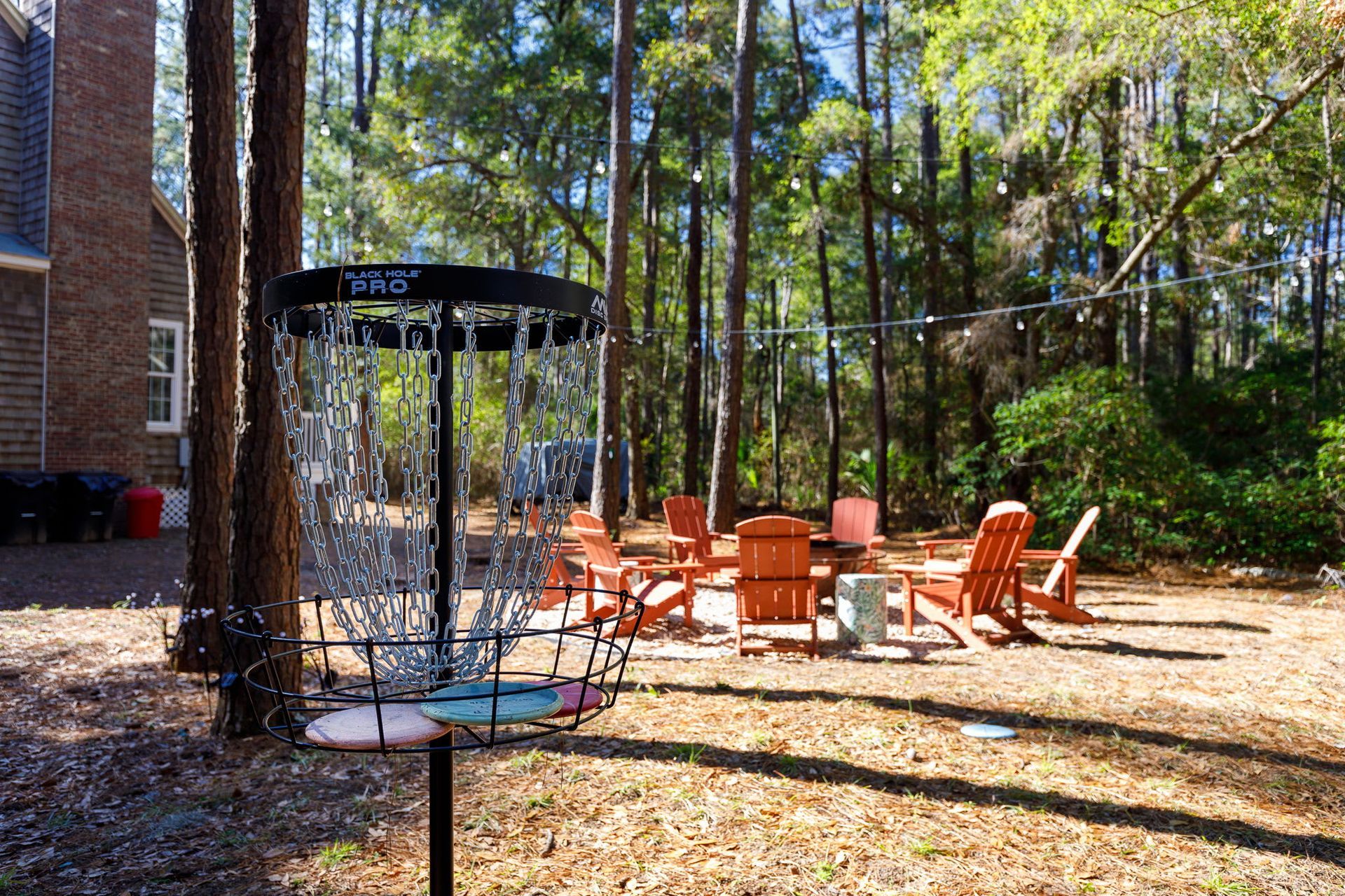 A frisbee golf basket is sitting in the middle of a backyard surrounded by trees.