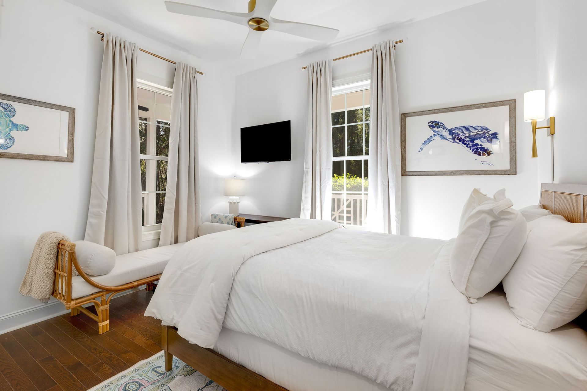 A bedroom with a king size bed , a bench , a television and a ceiling fan.
