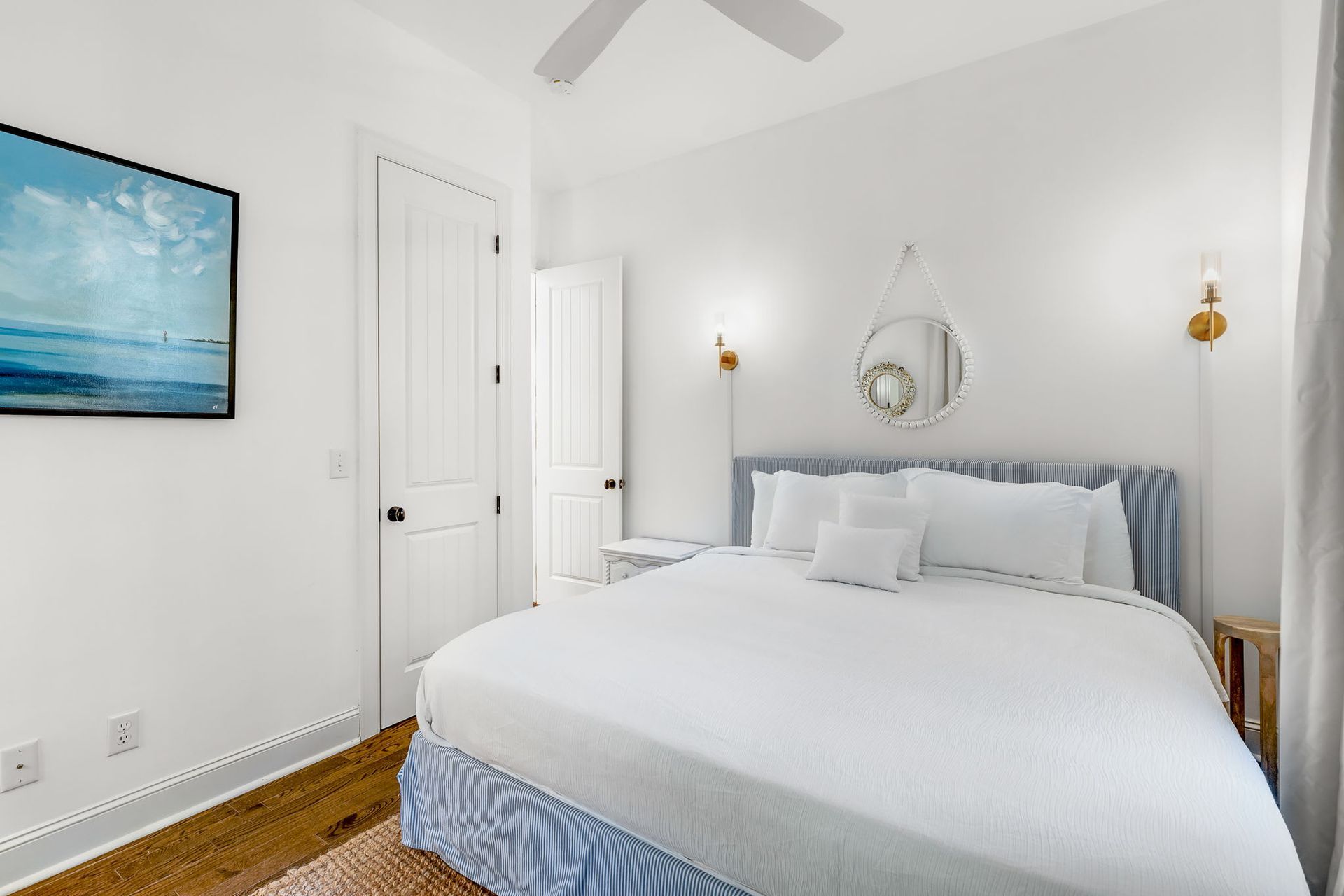 A bedroom with a king size bed , a painting on the wall and a ceiling fan.